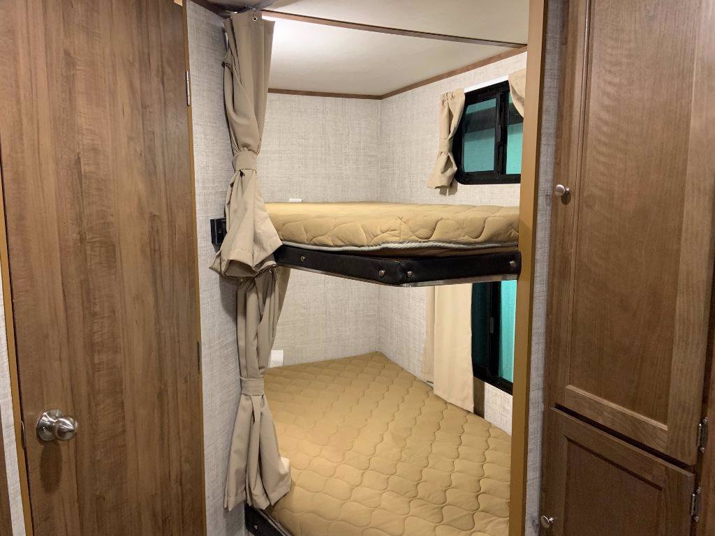 RV rental interior showing a bunk bed area with two beige mattresses, window, and privacy curtains, perfect for families.. Gulf Stream 25BHS 2020