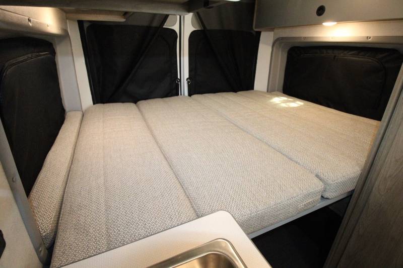 Comfortable modular bed in an RV rental, showing the spacious sleeping area with window covers and a sink counter.. Winnebago Solis 2021