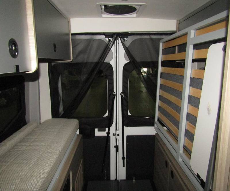 Interior of an RV rental: features a bed, overhead cabinets, and a folding slatted bed frame in the rear.. Winnebago Solis 2021