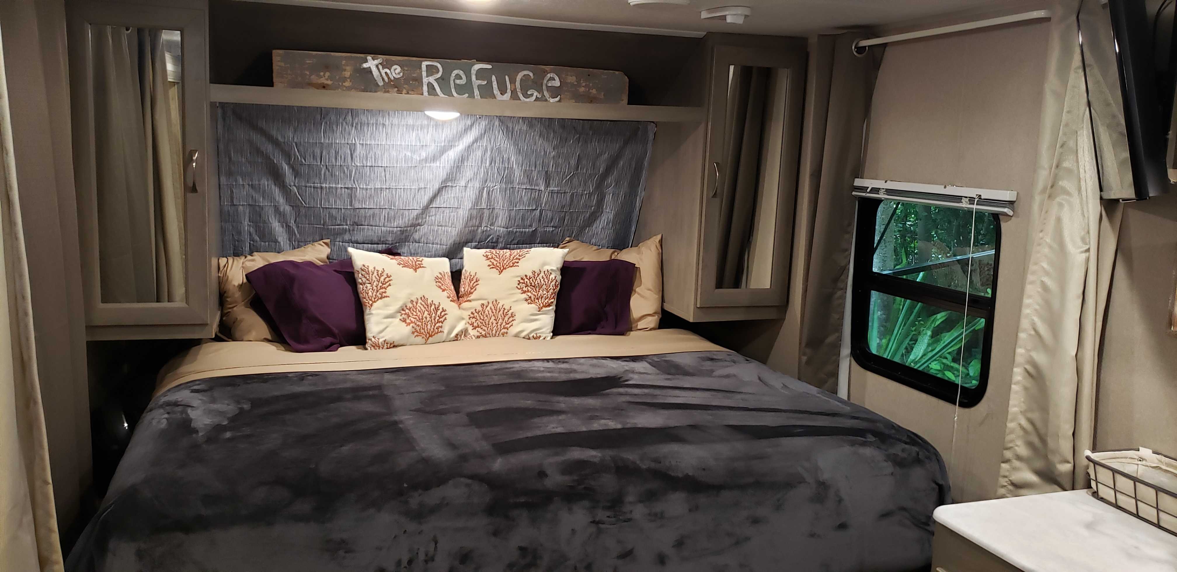 Cozy RV rental bedroom with a queen bed, purple and coral-patterned pillows, and a window view of lush greenery.. Palomino Other 2019