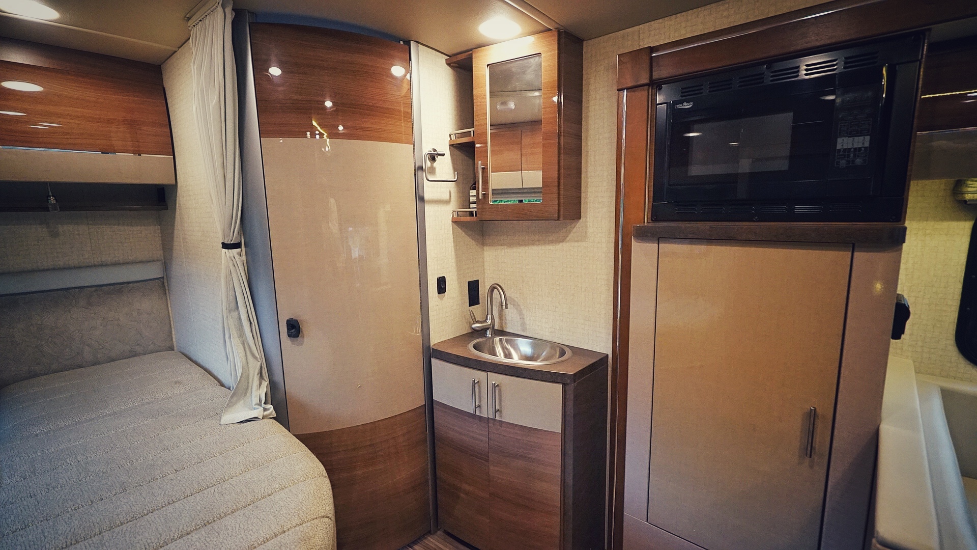 An RV rental interior displays a bed, small sink vanity, and mounted microwave, optimized for functional, compact travel.. Mercedes Sprinter 2017