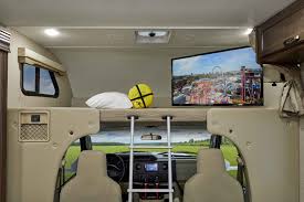 Inside an RV rental: front cab, overhead bunk with ladder, TV, & scenic road view. Ideal for comfortable travel.. Thor Freedom Elite 2020