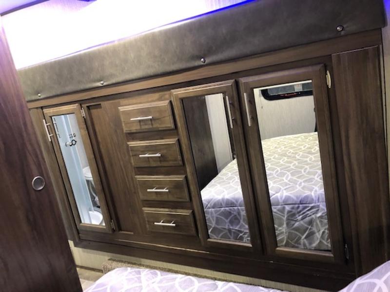 RV rental interior showing a dark wood storage cabinet with mirrored doors and drawers, reflecting the bed.. Forest River Cherokee Arctic Wolf 2019