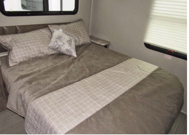 A spacious RV rental bedroom featuring a large bed with neutral bedding, a headboard, and an emergency exit window.. Entegra Coach odyssey 2020