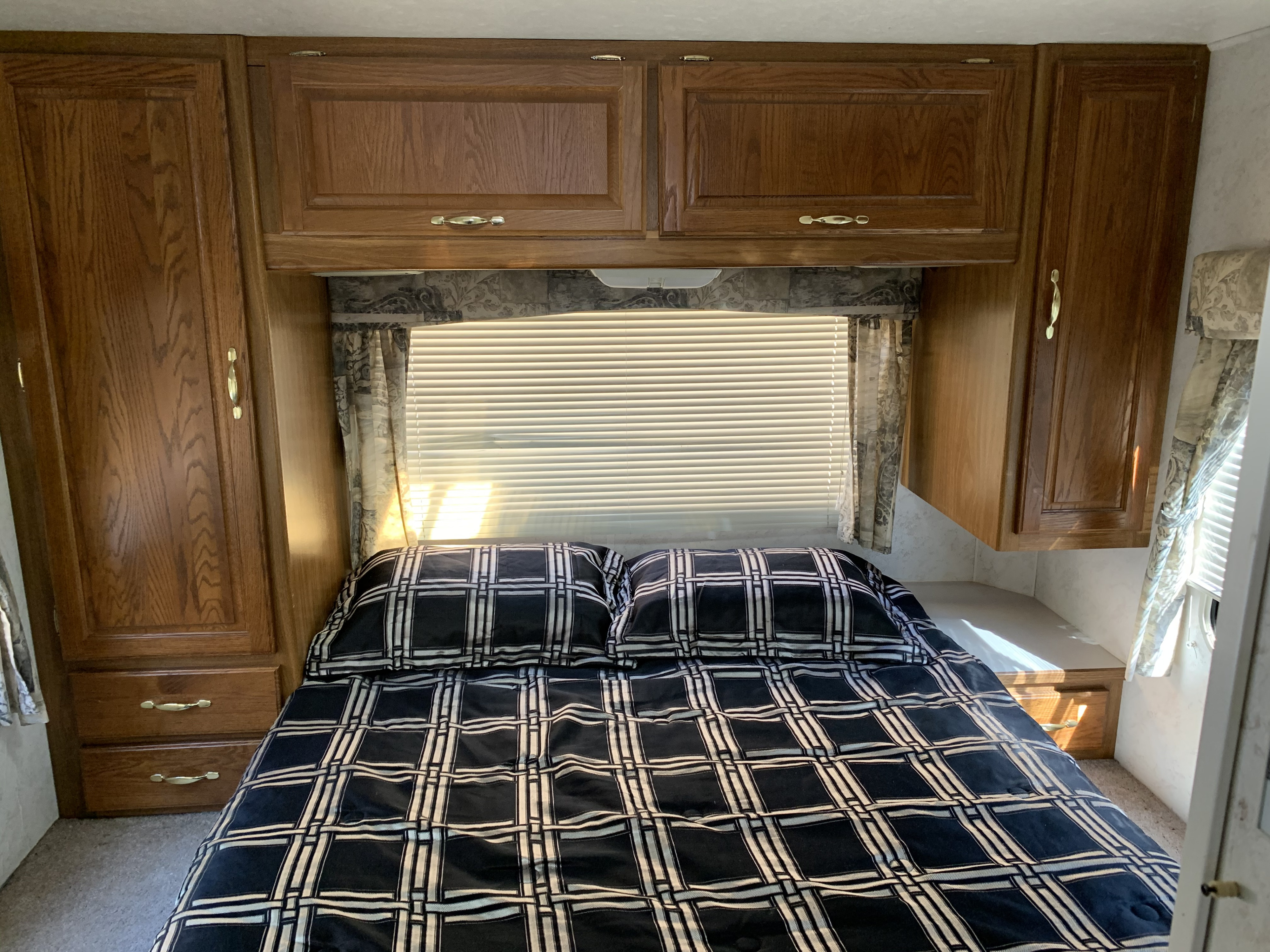Comfortable RV rental bedroom with plaid bedding, wooden cabinets, and sunlit window with blinds.. Majestic Leisure Craft E350 2001
