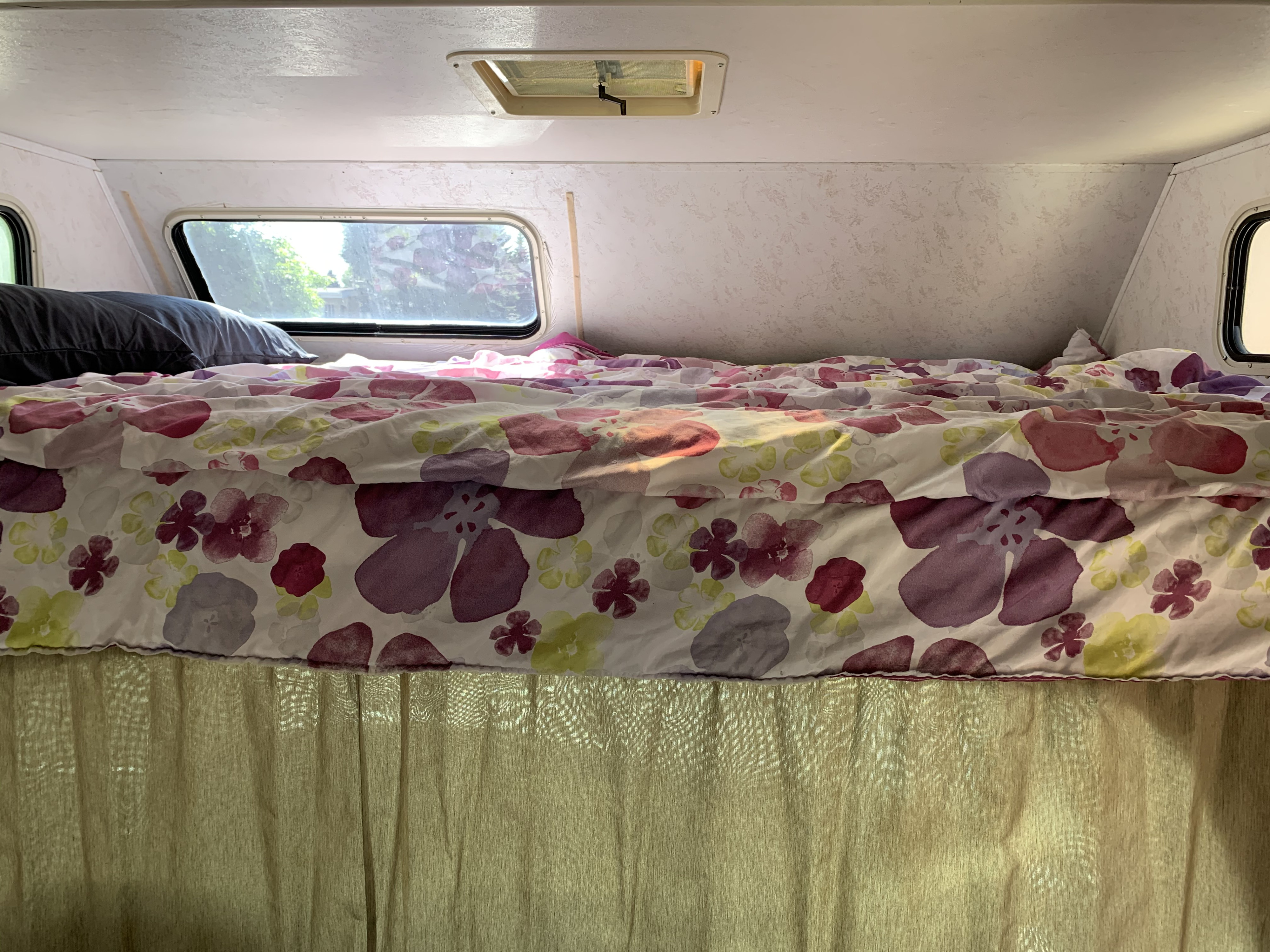 Inside an RV rental: a comfortable bed with a floral comforter, pillow, and bright windows for a restful sleep.. Majestic Leisure Craft E350 2001