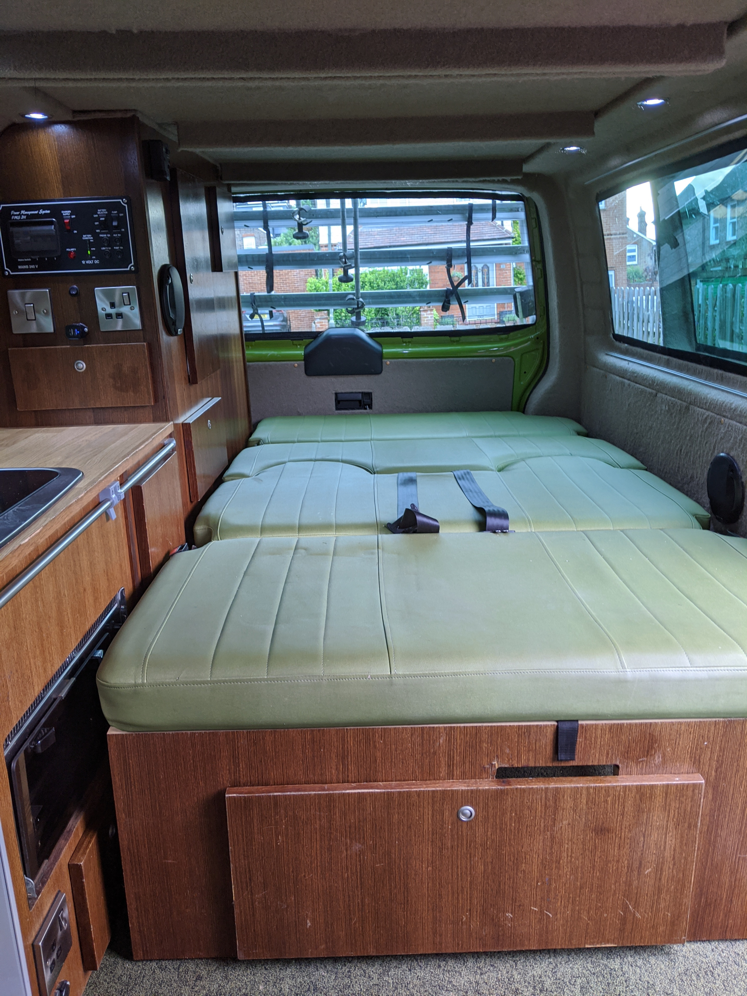 Experience comfort in this RV rental: a cozy camper van interior with green convertible seating/bed, wood cabinets, and rear window view.. Volkswagen Other 2007