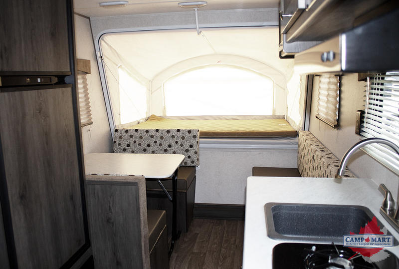 A detailed look inside an RV rental, showing a comfortable pop-up bed, dinette seating, and compact kitchen area.. Grand River 16RB 2019