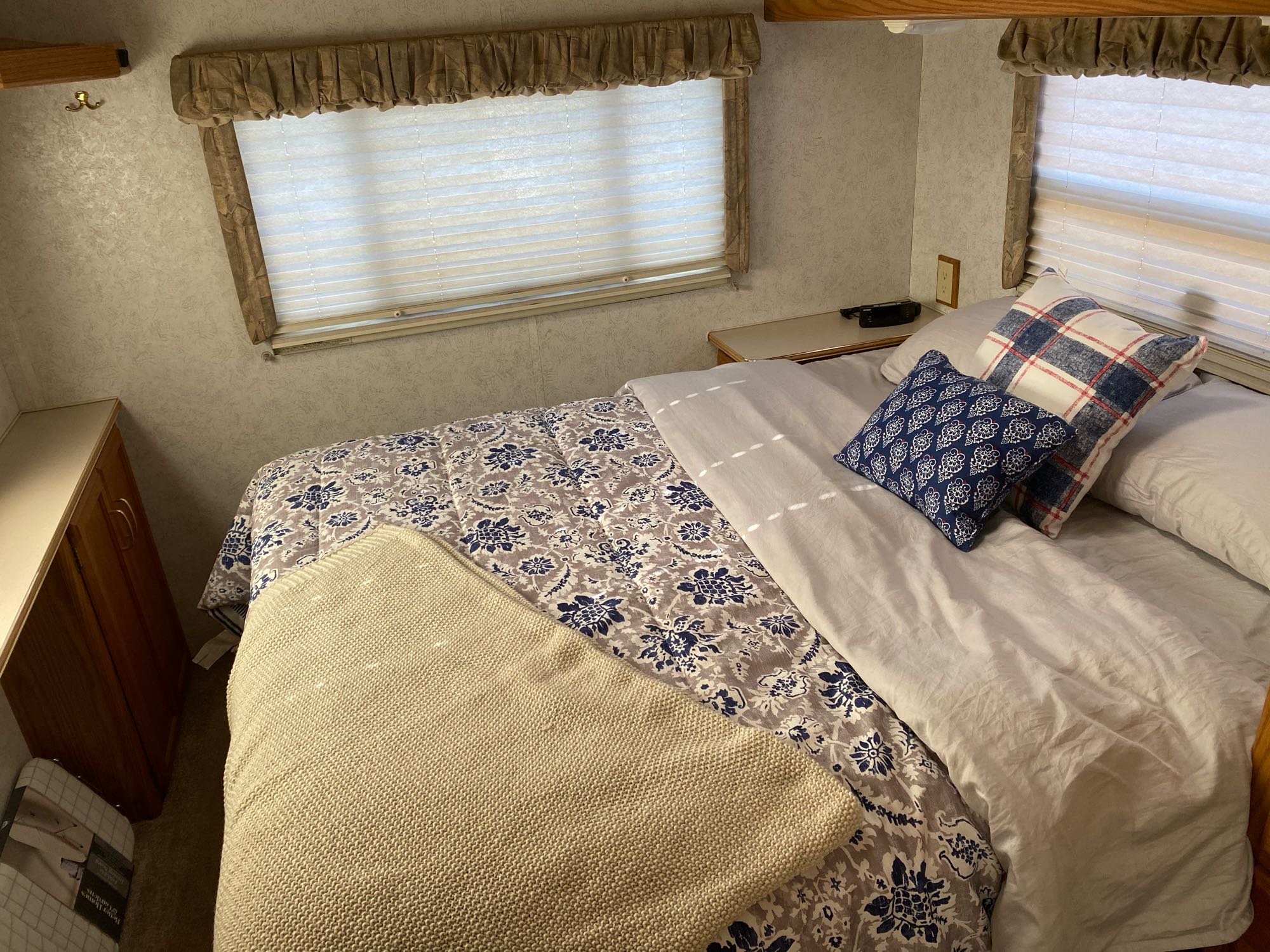 Cozy rv rental bedroom interior, featuring a comfortable bed with blue patterned bedding, throw pillows, and a window.. Itasca Spirit 2000