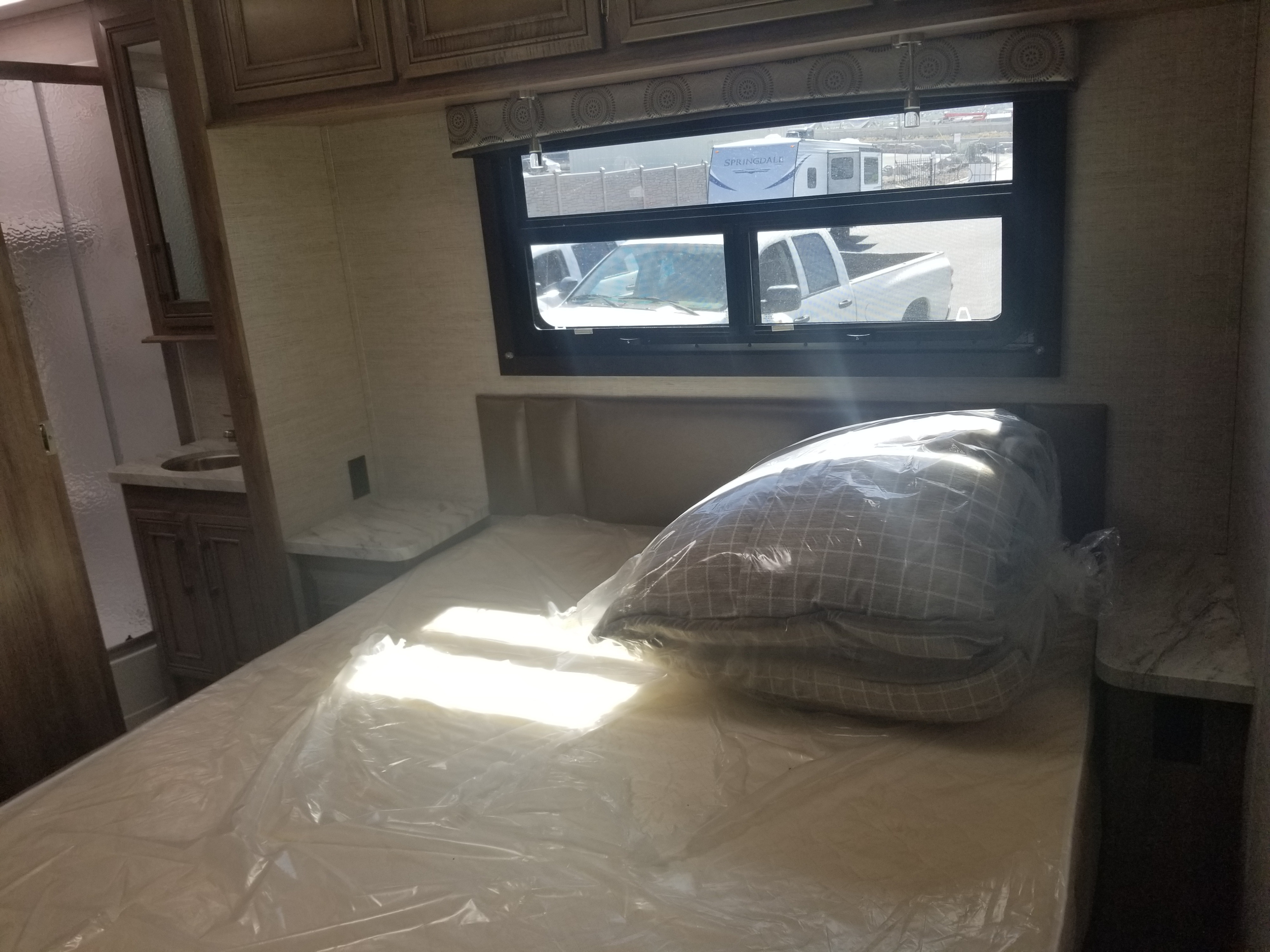 Cozy RV rental bedroom featuring a new bed in plastic. Outside, another RV and truck are visible through the window.. Entegra Coach Other 2021