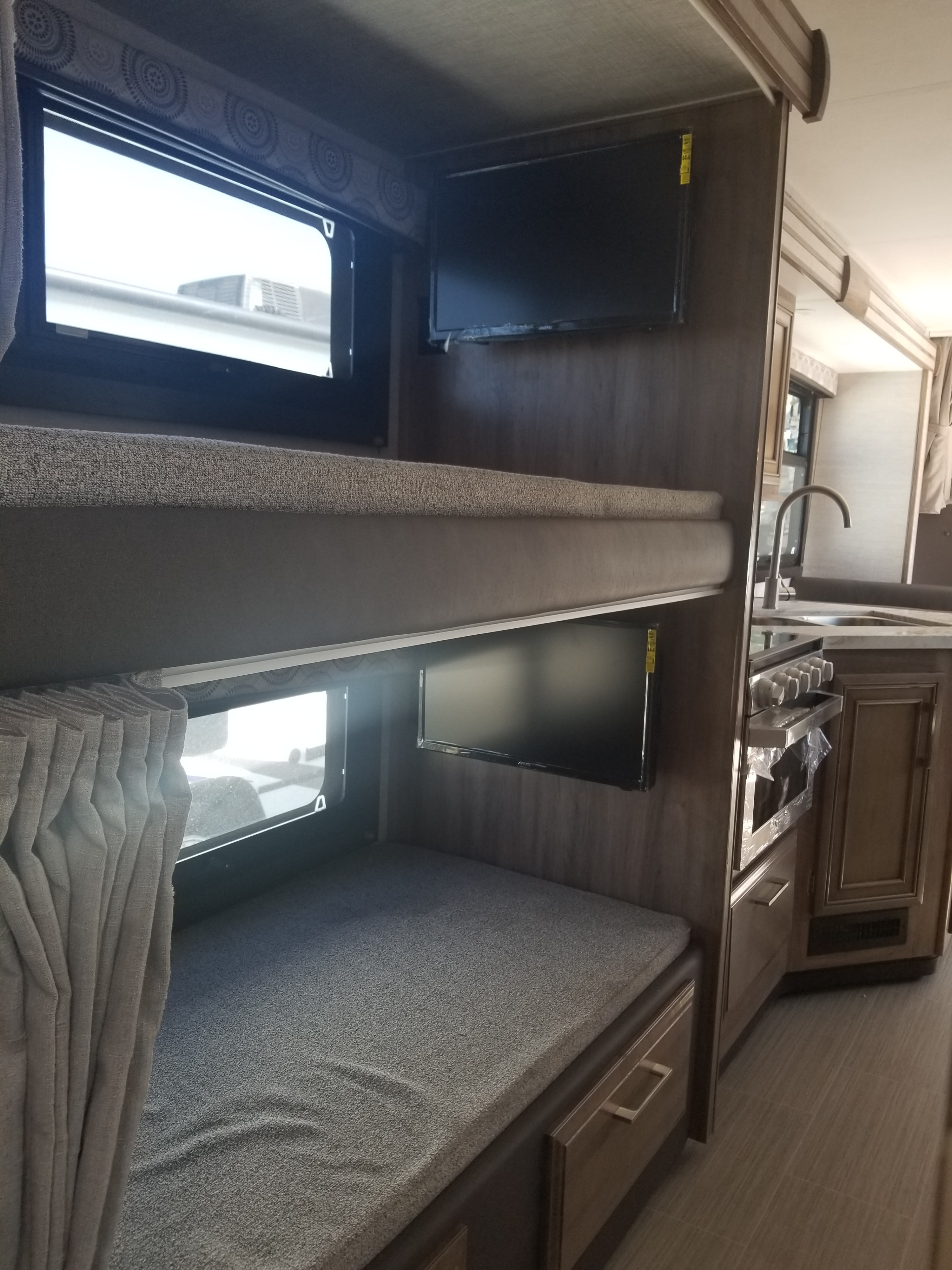 Inside an RV rental: comfortable bunk beds with individual TVs and a compact kitchen area with a sink and stove.. Entegra Coach Other 2021
