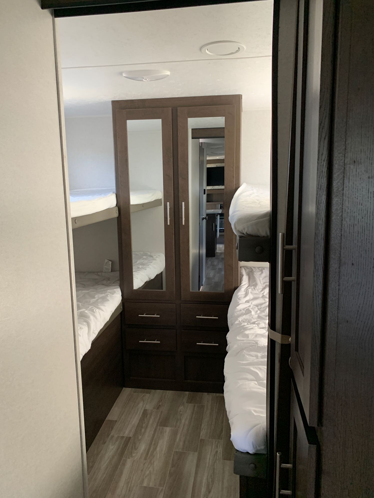 An RV rental bunk room shows two white bunk beds and a mirrored cabinet, reflecting the living area beyond.. Forest River Salem Cruise Lite 2020