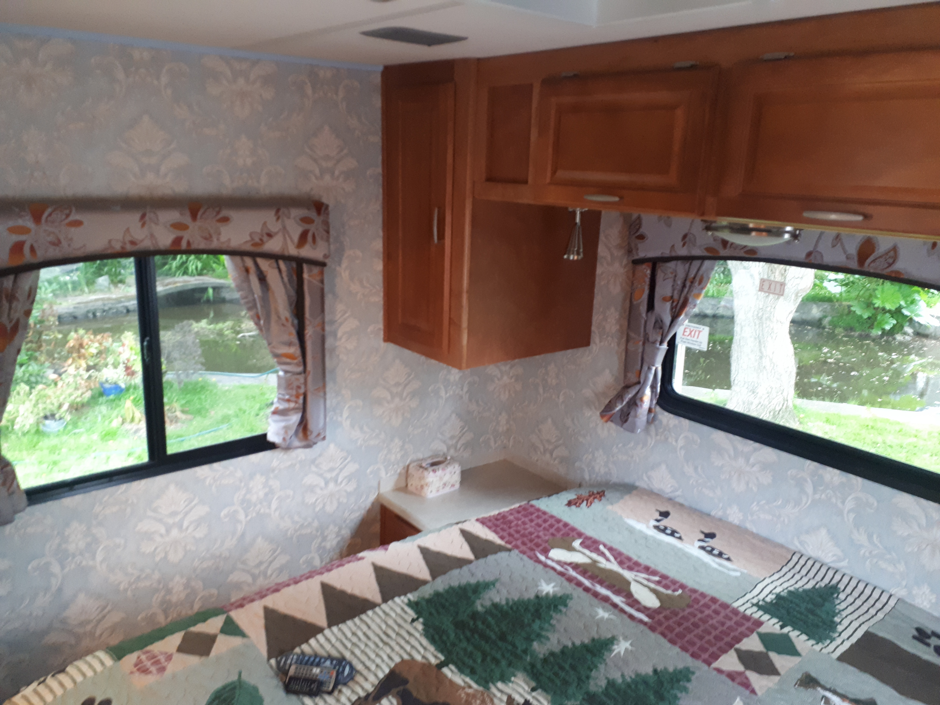Cozy RV rental bedroom with a nature-themed quilt, wooden cabinets, and windows overlooking a pond.. Other Other 2009