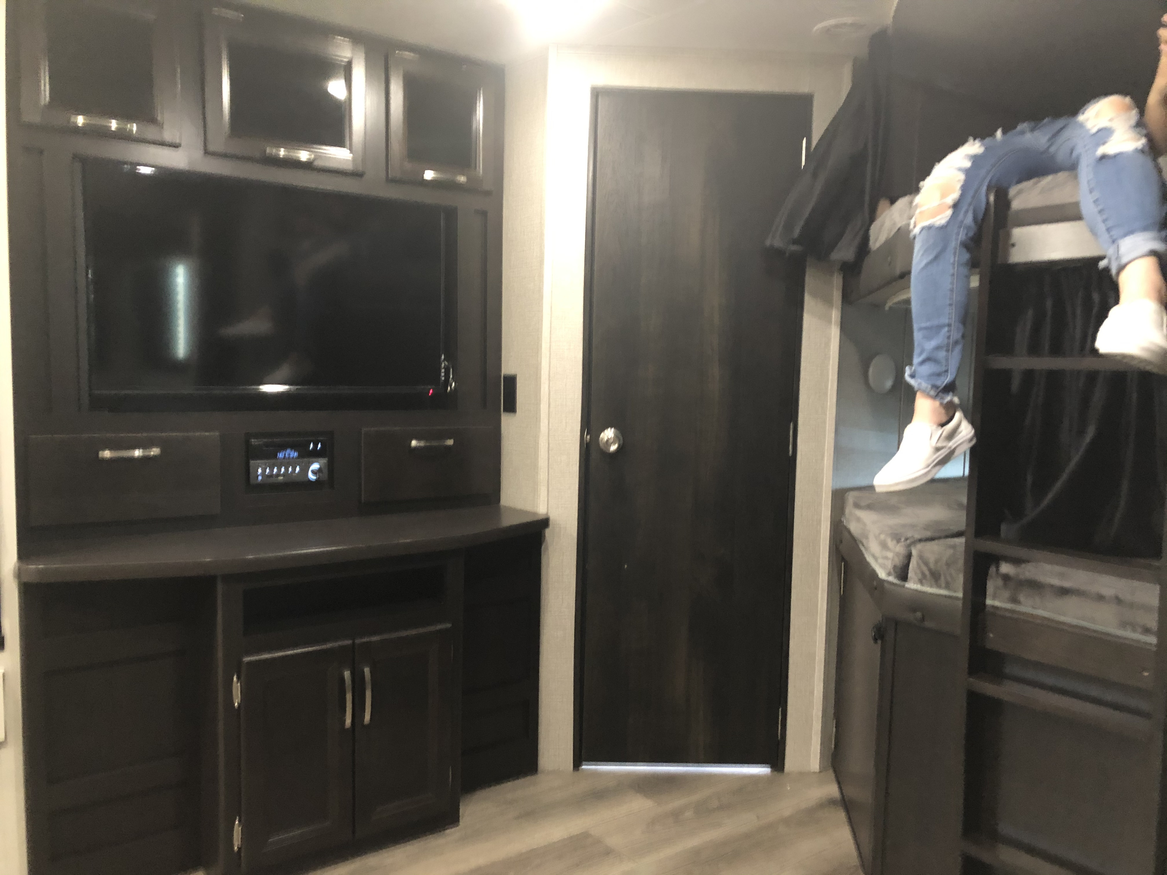 Step into this modern RV rental! Features include a dark wood entertainment center, TV, door, and cozy bunk beds.. Jayco Jay Feather 2020