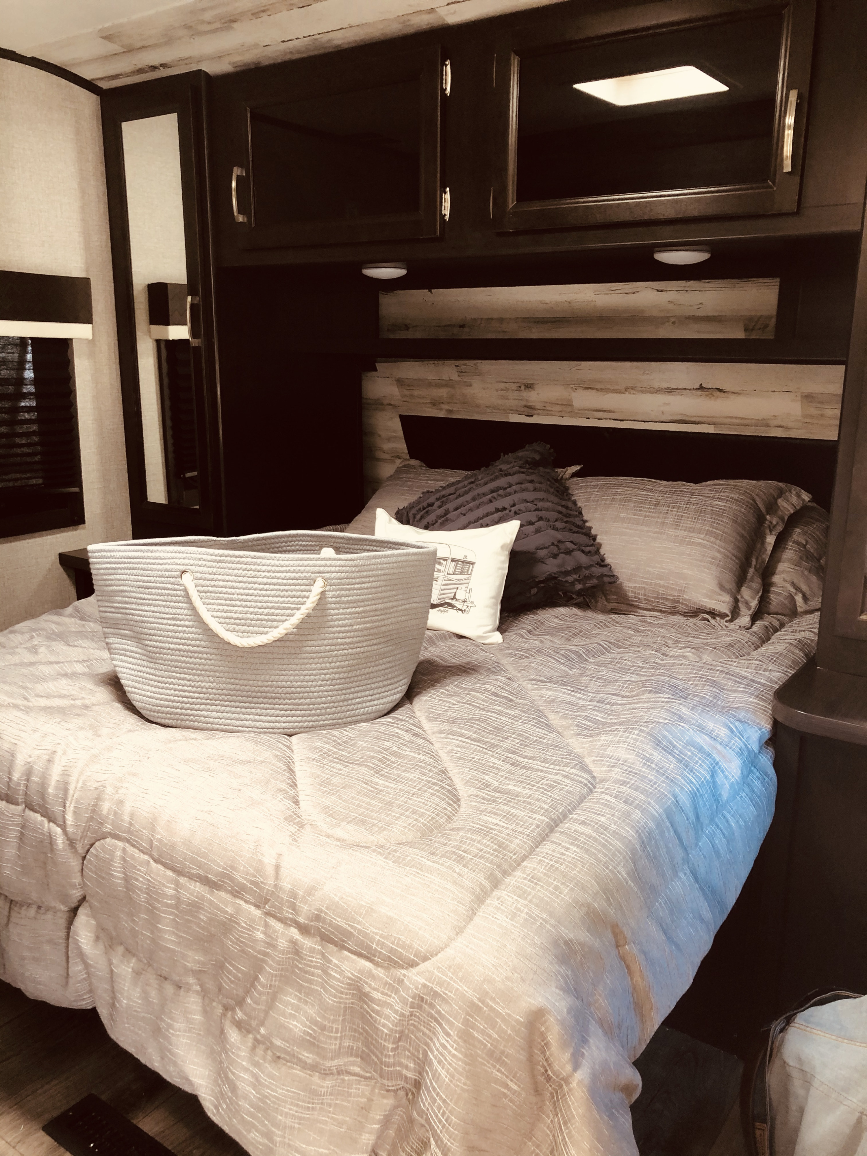 Comfortable RV rental bedroom featuring a cozy bed, woven storage basket, and modern overhead cabinets.. Jayco Jay Feather 2020