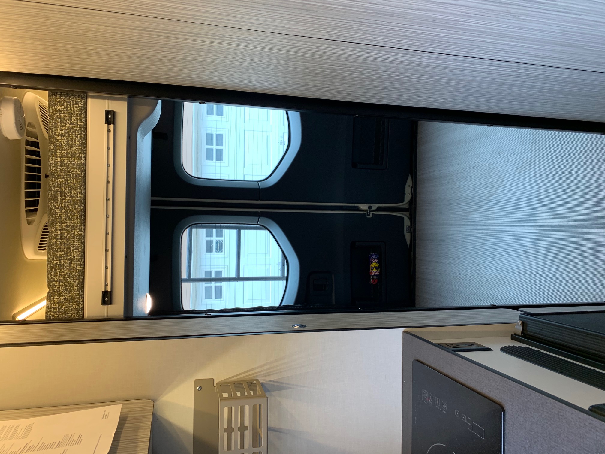 A bright RV rental interior showing a bed area, rear doors with windows, and a compact kitchen counter.. Winnebago Revel 2020