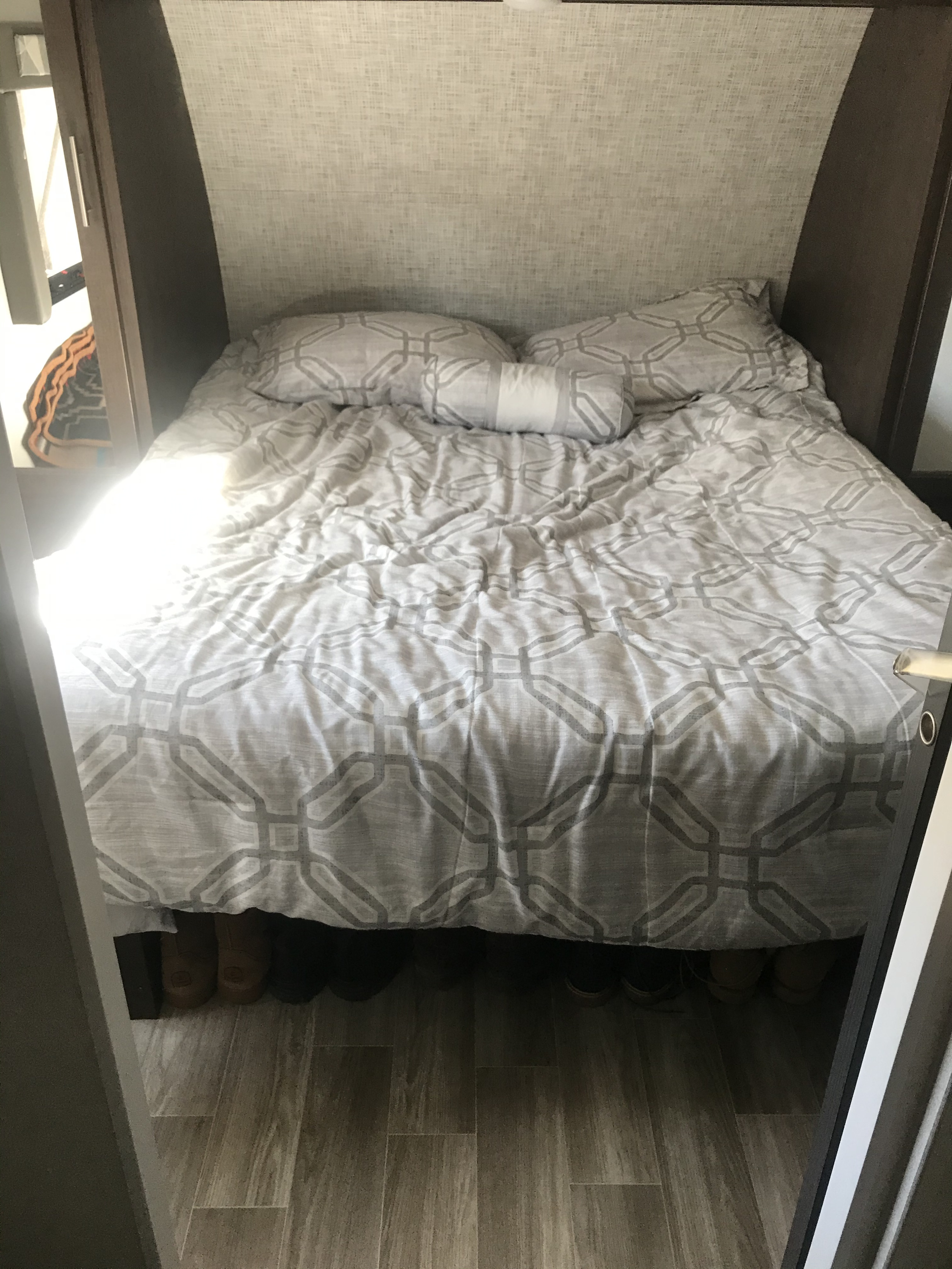 RV rental bedroom with a cozy bed, grey patterned bedding, and a textured headboard. Shoes are visible on the floor below.. ForestRiver CruiseLite 2019