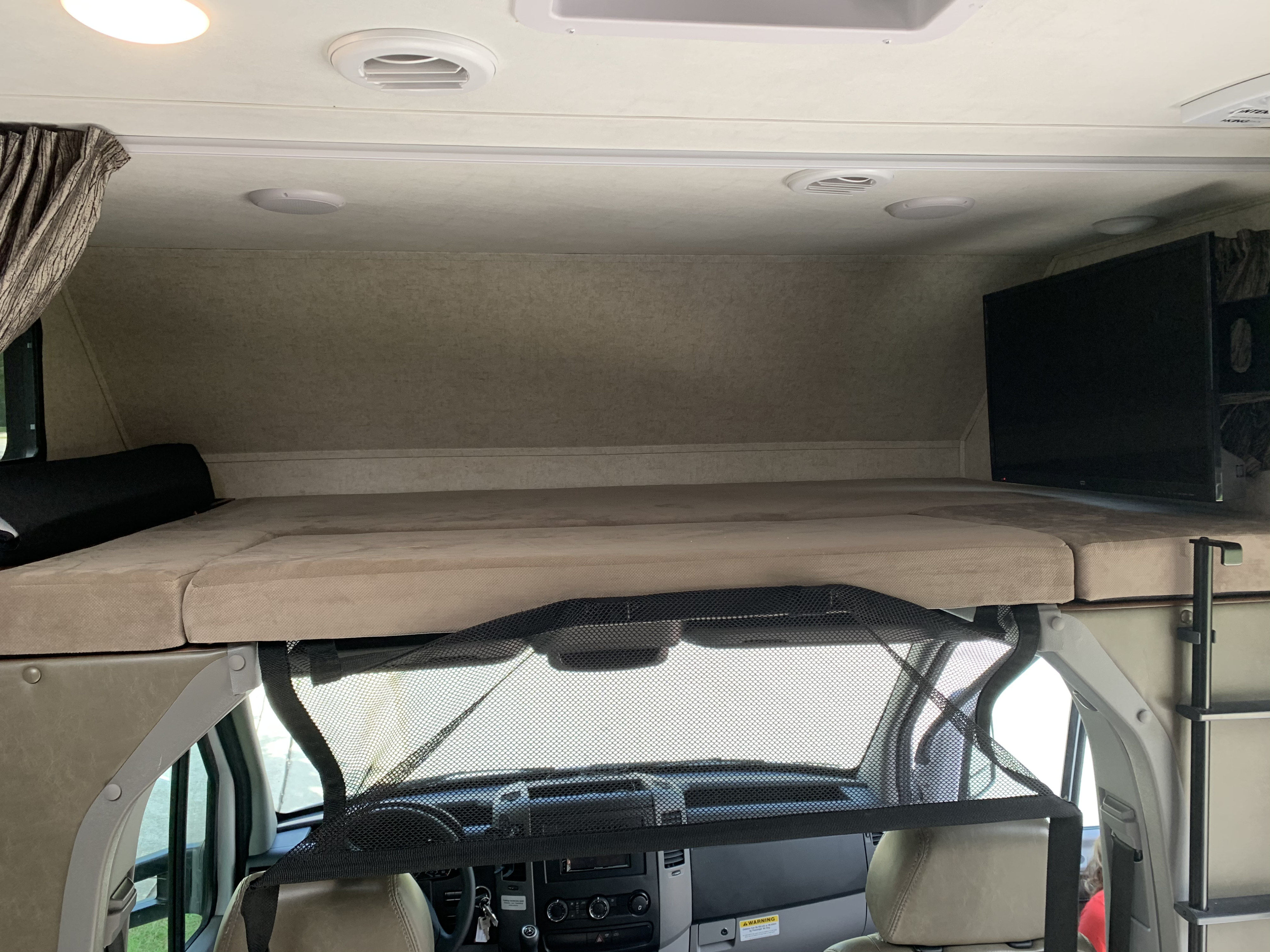 RV rental interior: view of the overhead bunk bed with cushions, TV, and a safety net above the front cab.. Forest River Sunseeker 2019