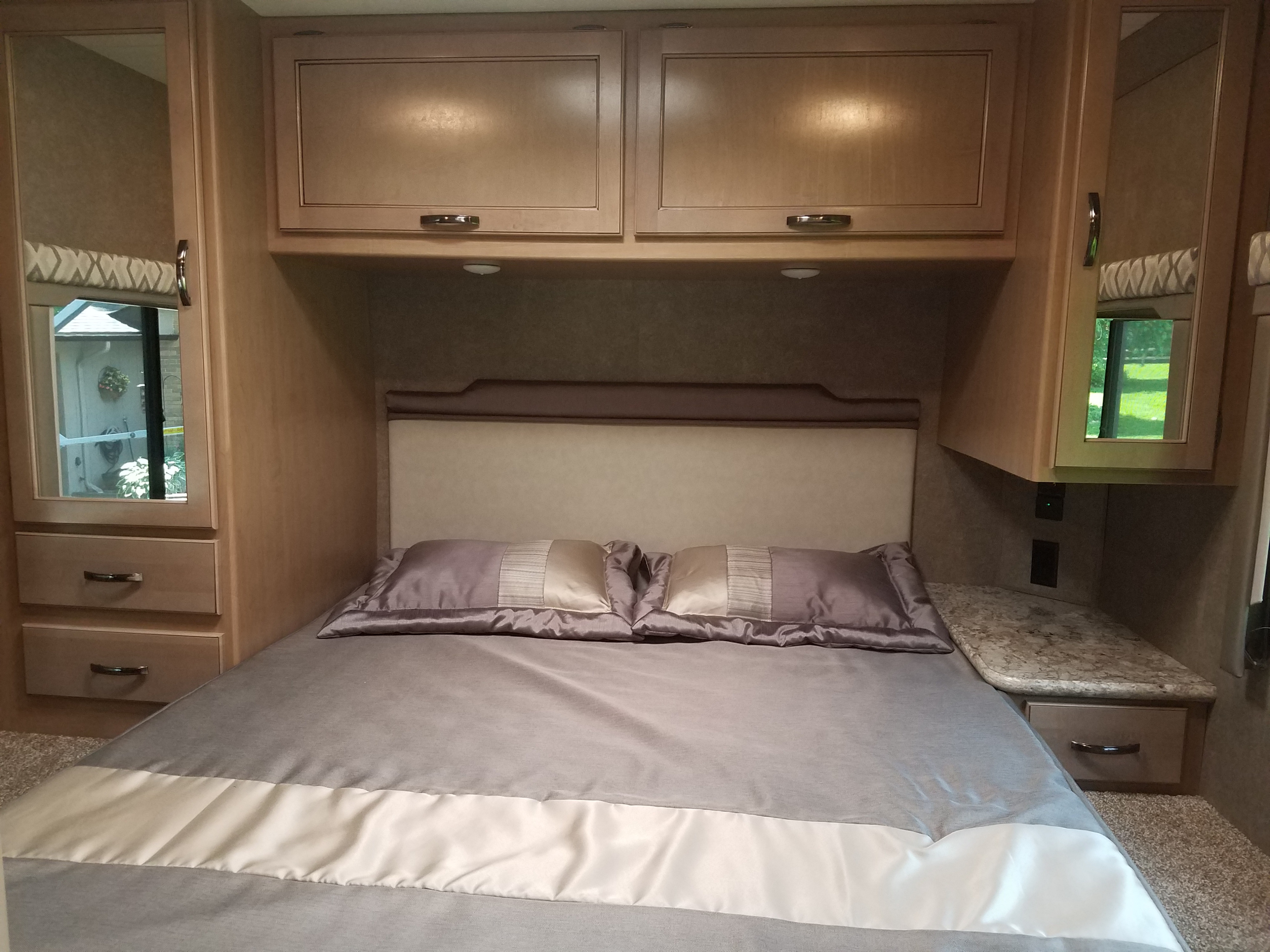 Cozy RV rental bedroom featuring a comfortable bed, overhead cabinets, and built-in storage on both sides.. Thor Four Winds 2020