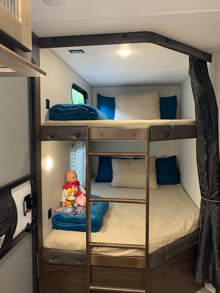 Inside an RV rental, discover cozy bunk beds with a ladder, bright lighting, and privacy curtain, perfect for a family trip.. Forest River Cherokee Grey Wolf 2021