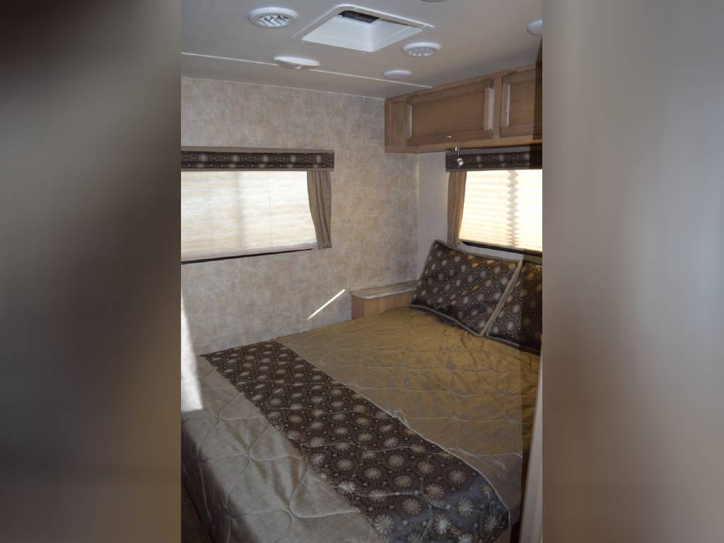 Comfortable RV rental bedroom featuring patterned bedding, window blinds, and overhead cabinets for a cozy stay.. Gulf Stream Conquest 2018