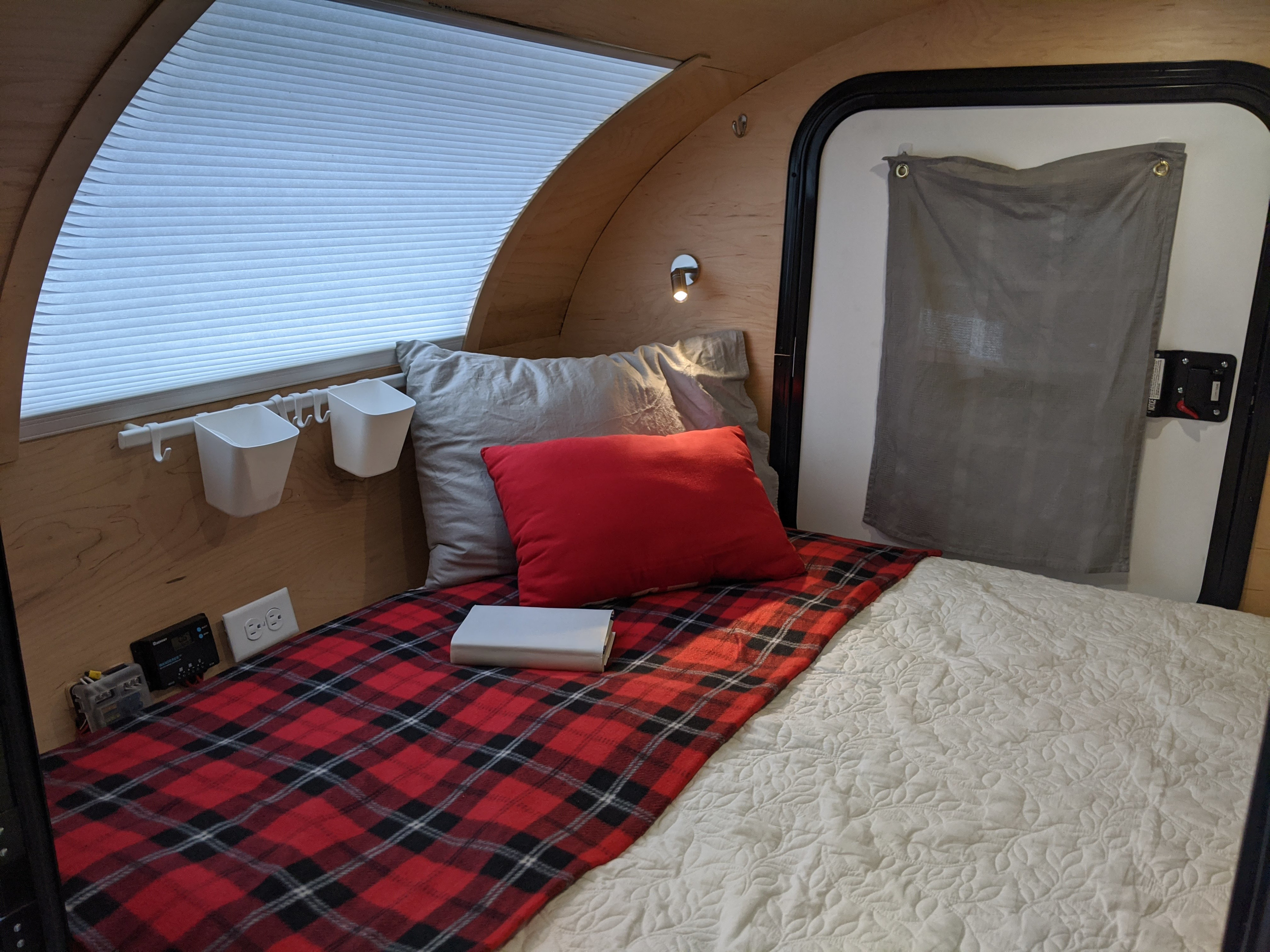RV rental interior: a comfy bed with red plaid blanket, white quilted comforter, window shade, and compact amenities.. Custom Teardrop Camper 2019