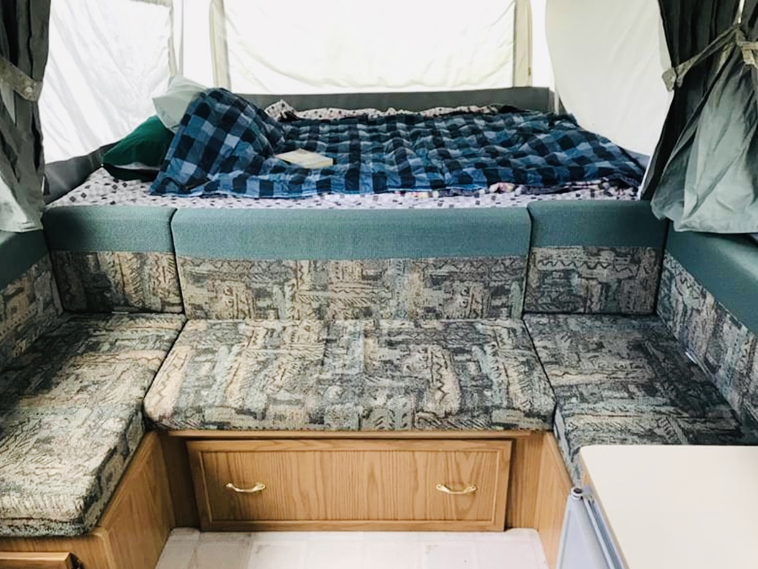 Pop-up camper RV rental interior: cozy bed, patterned U-shaped dinette seating, and wood cabinets. Great for camping!. Coleman GrandTourMesa 1999