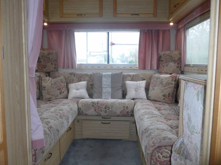 Cozy RV rental interior featuring a floral U-shaped seating area with decorative pillows, pink curtains, and wooden cabinets.. Peugeot Boxer Elddis Auto Stratus EB 1999