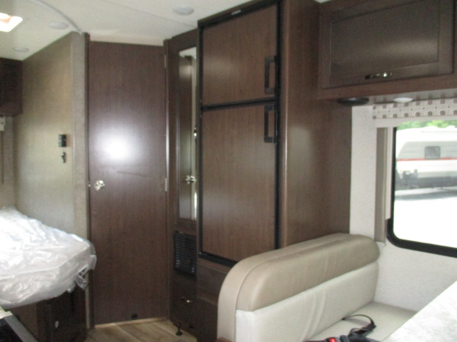 Inside an RV rental: features a bed, refrigerator, and dinette seating with a window view. Wood finishes throughout.. Thor Motor Coach Four Winds 2021