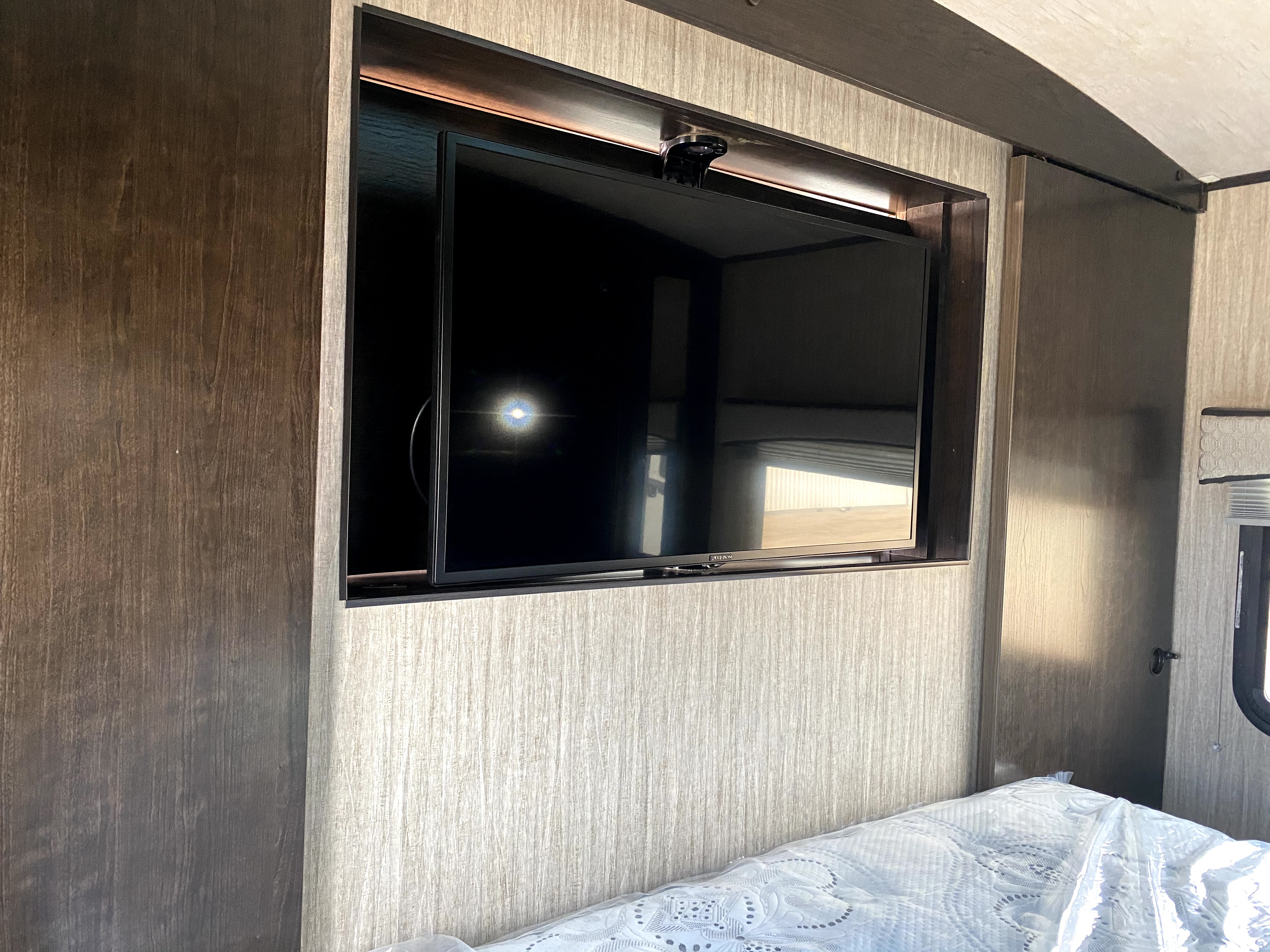 Inside an RV rental, a bedroom features a mounted TV with an overhead camera and lighting, next to a bed.. Cruiser RV Shadow Cruiser 2019