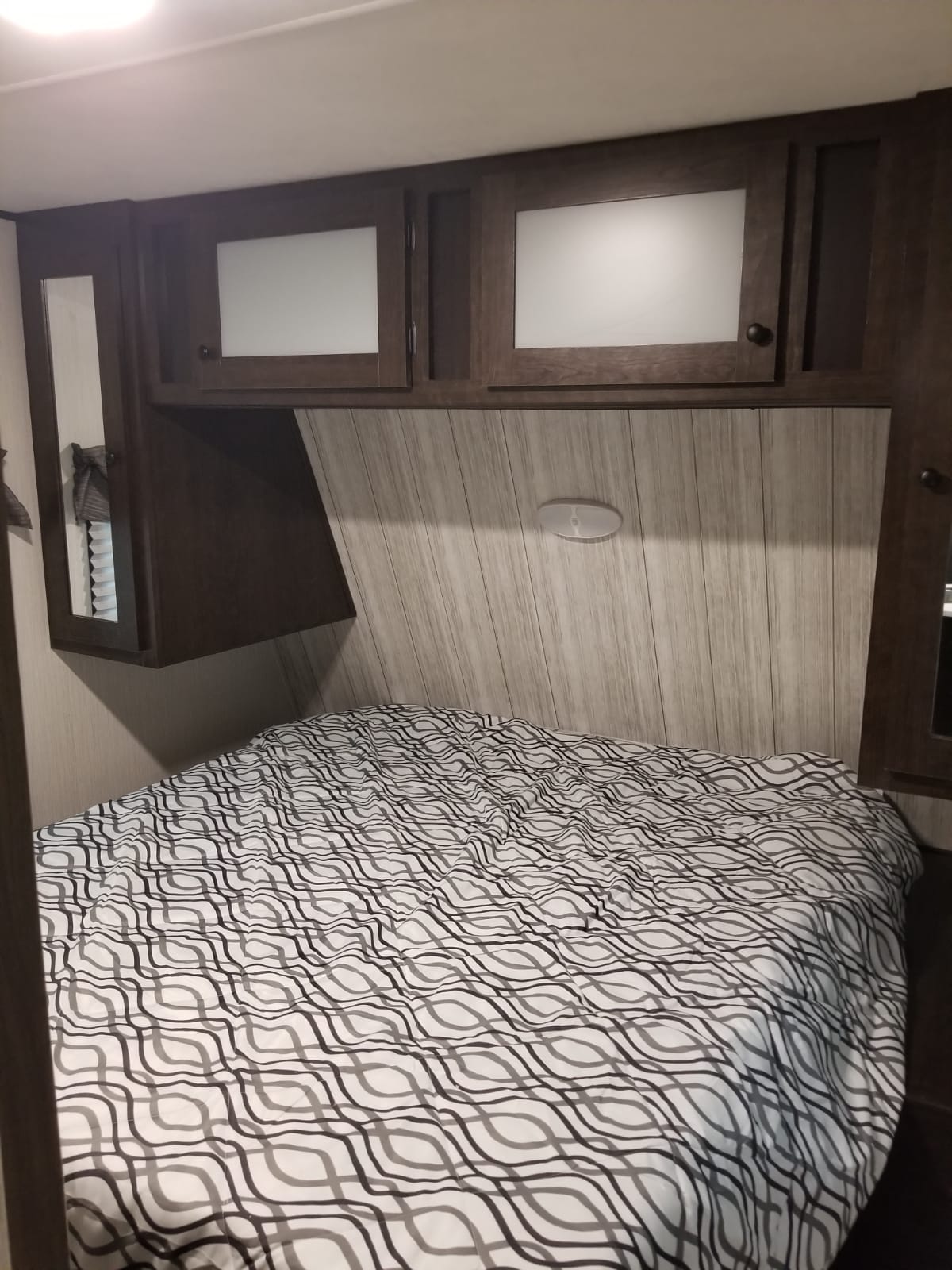 An RV rental bedroom features a comfy bed with a wavy patterned comforter, dark wood cabinets, and light wood walls.. Heartland Pioneer 2020