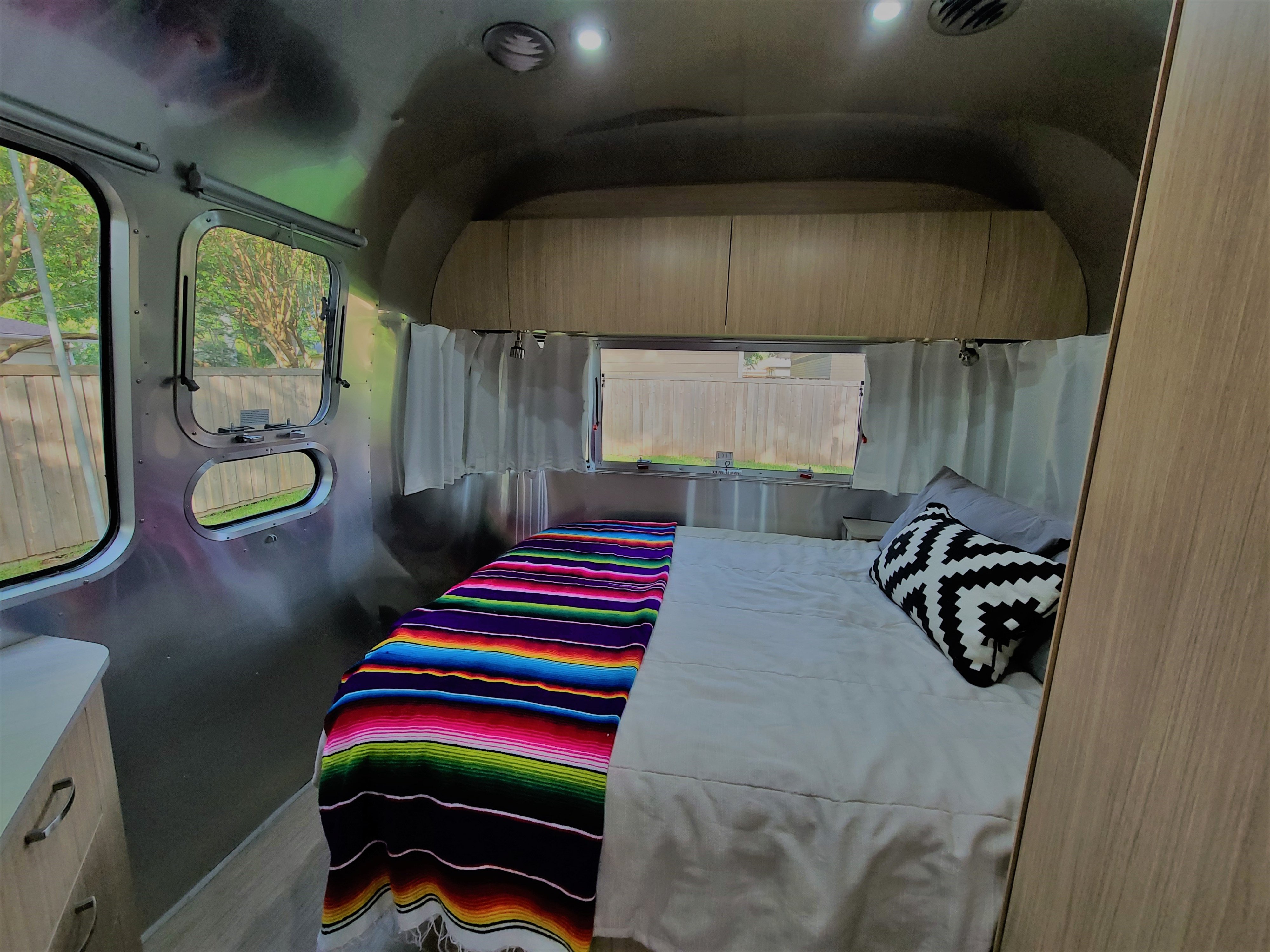 Cozy Airstream **rv rental** bedroom with a colorful serape blanket, wood cabinets, and signature large windows.. Airstream Flying Cloud 2020