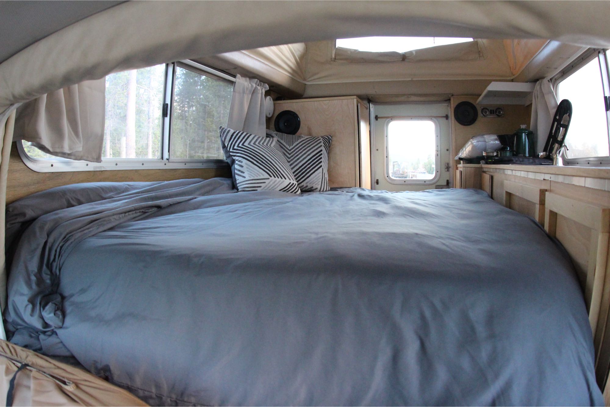 Cozy RV rental interior features a large bed, windows overlooking a forest, and a compact living space.. Chinook Toyota 1976