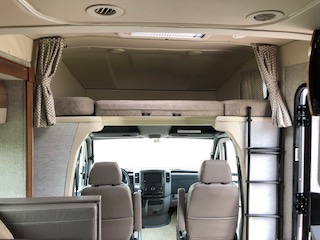Experience comfort in this RV rental! Interior view showing the driver's cab, front seats, and an overhead bunk bed with a ladder.. Winnebago View 2018
