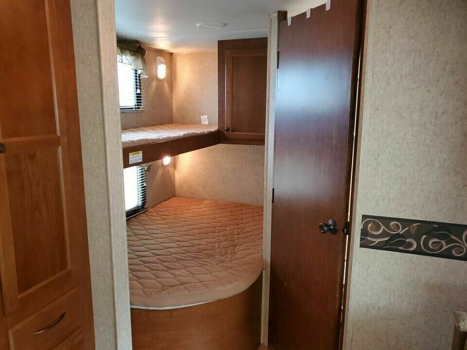 RV rental: Interior view of bunk beds with mattresses, wall sconces, windows, and a wooden door, ideal for travel.. Heartland Prowler 2012