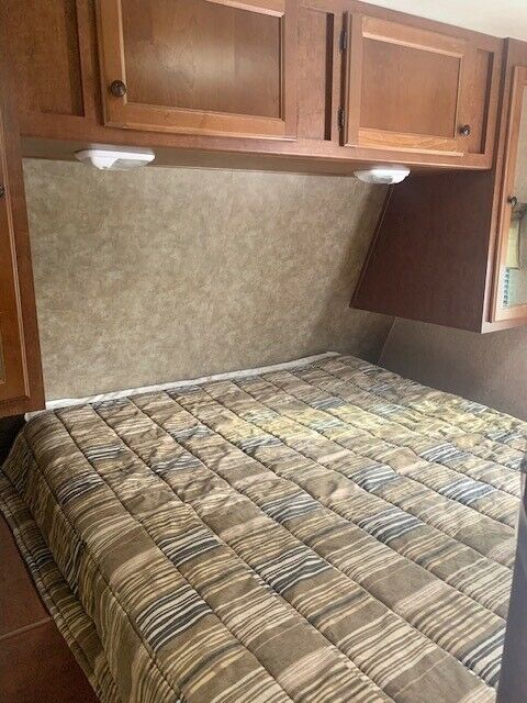 RV rental bedroom with comfortable striped bed, overhead cabinets, and lighting.. Heartland Prowler 2012