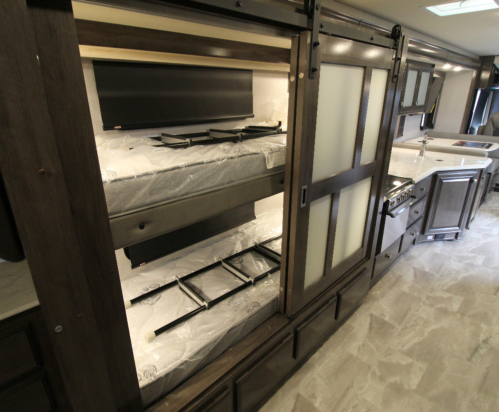 Step inside this spacious rv rental featuring modern bunk beds, a ladder, and a sleek kitchen setup.. Fleetwood Flair 2022