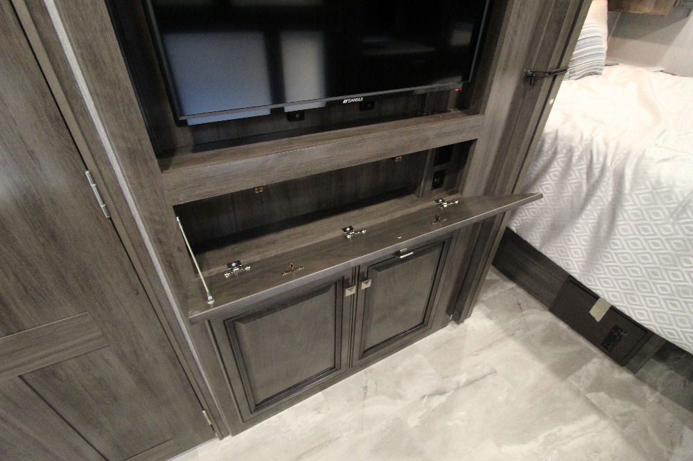 RV rental interior: A mounted TV sits above an open media console with outlets and lower cabinets, adjacent to a bedroom area.. Fleetwood Flair 2022