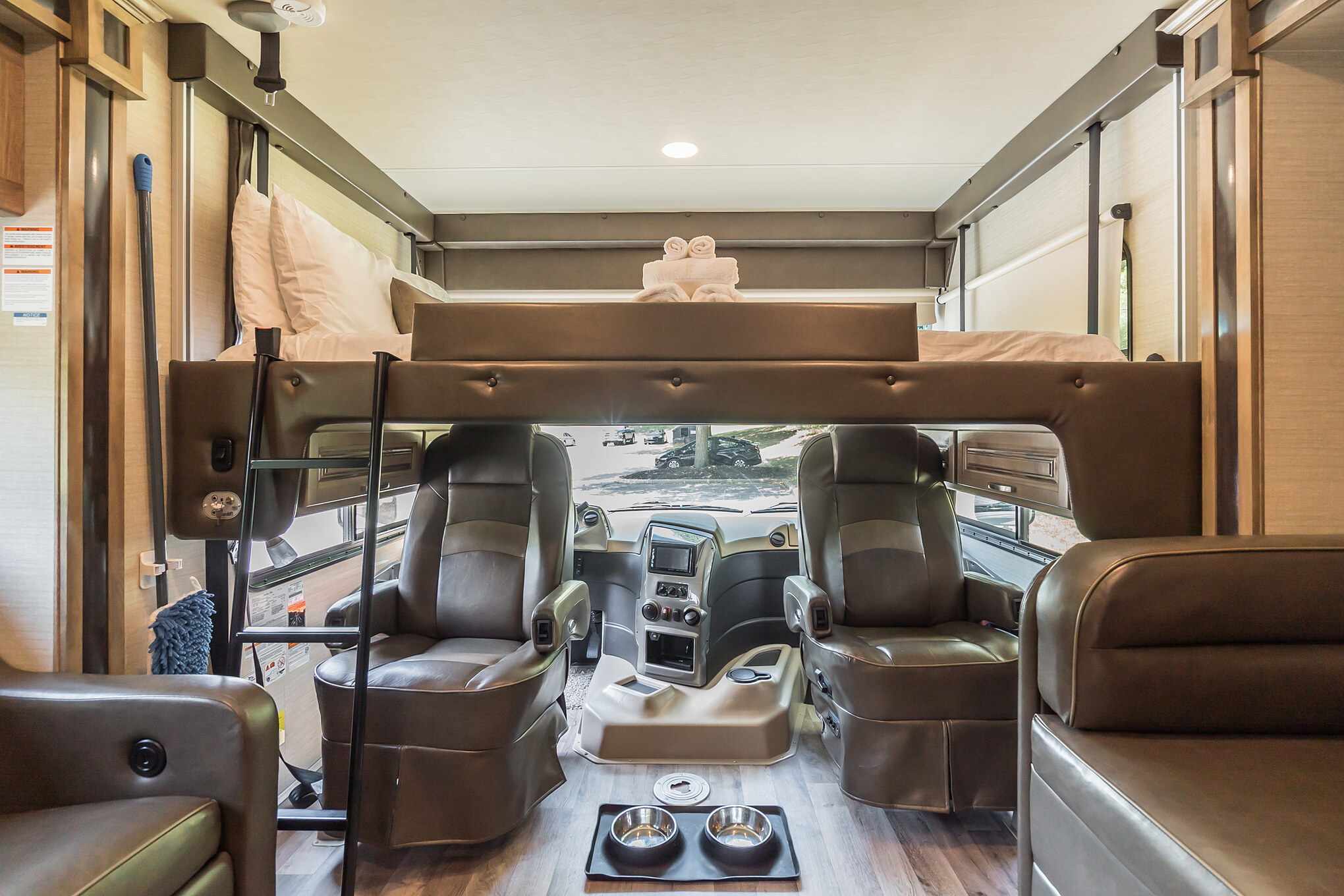 RV rental interior: overhead bunk bed, driver's cockpit with pet bowls on floor. A cozy, ready-to-travel motorhome.. Jayco Precept 2019