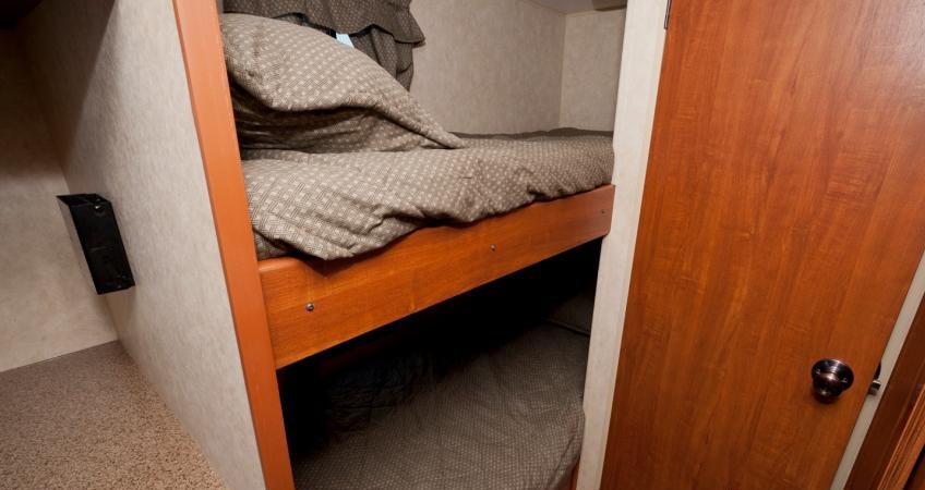 Cozy bunk beds in an RV rental interior, featuring patterned bedding and efficient space, perfect for compact sleeping arrangements.. Travel Lite Cobblestone I17 2014