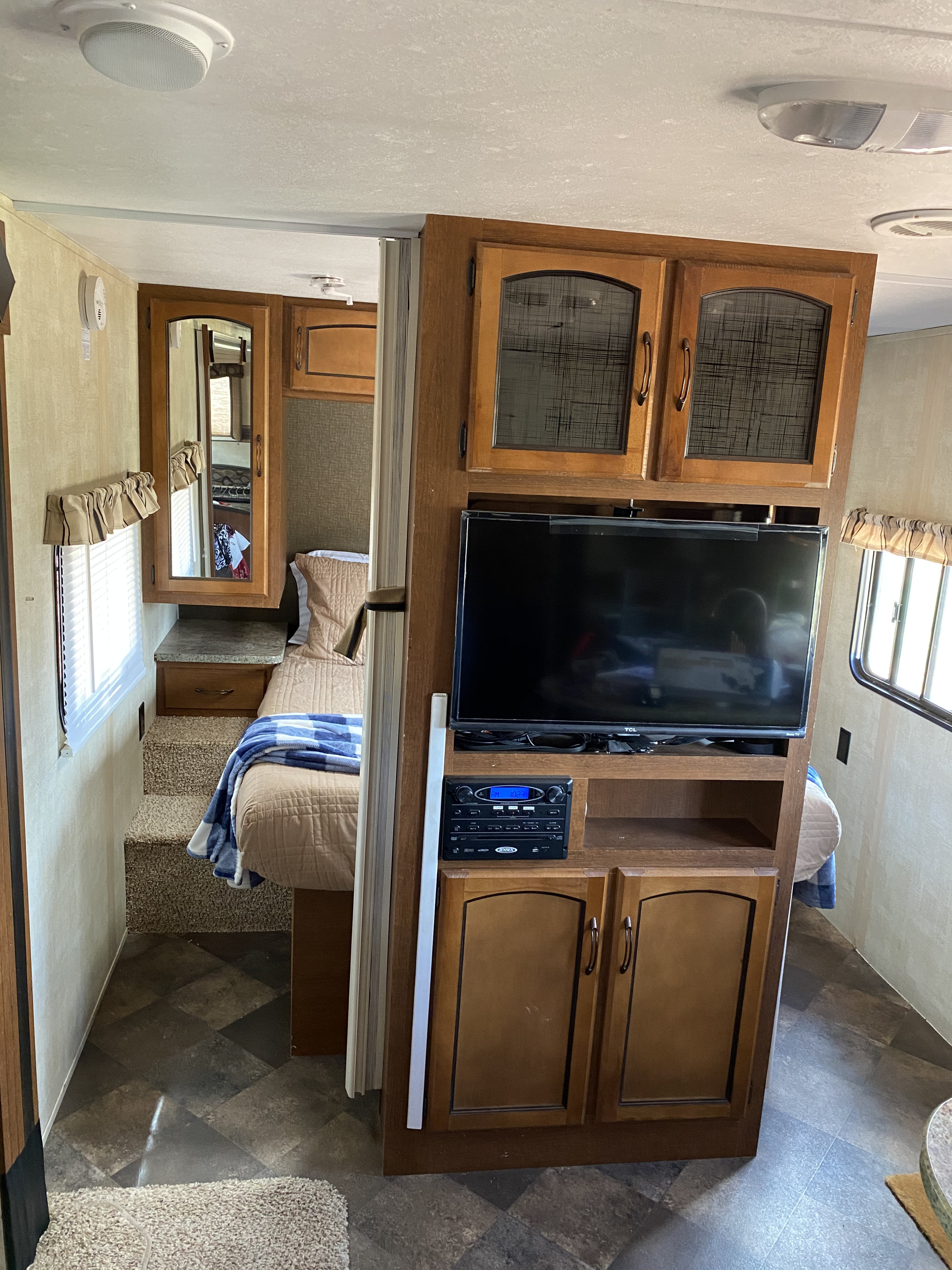 An RV rental interior revealing a functional entertainment center with TV, and a cozy step-up bedroom area.. Keystone Springdale 2014