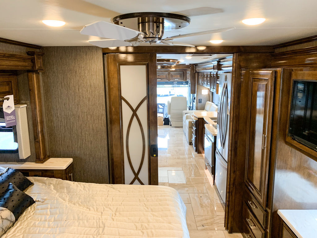 Luxury RV rental interior, featuring a bedroom with textured walls and ceiling fan, connecting to a full living space.. Thor Motor Coach Tuscany 2019