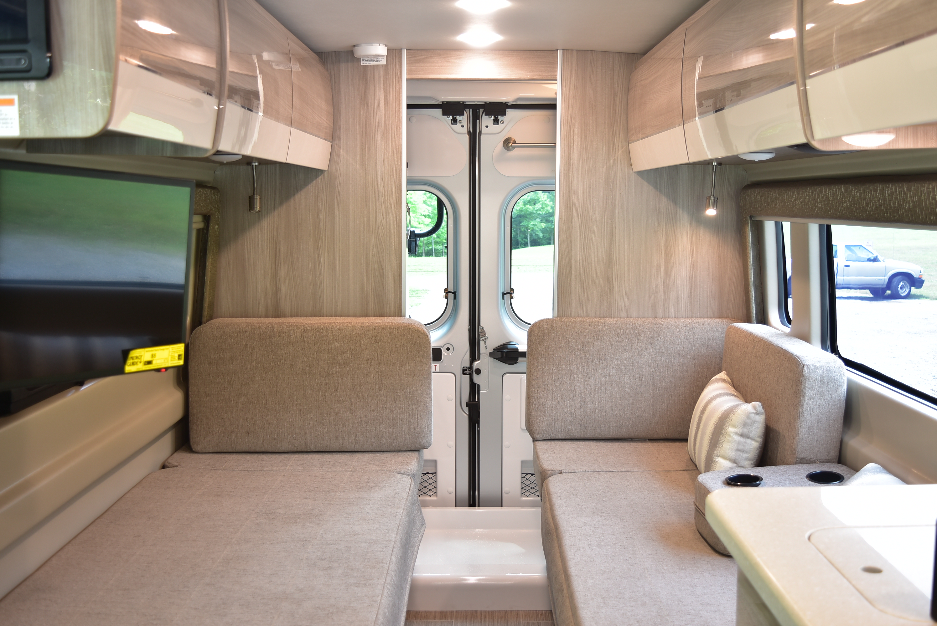 Spacious RV rental interior with convertible bench seating, overhead storage, and rear doors open to nature.. Other Other 2021