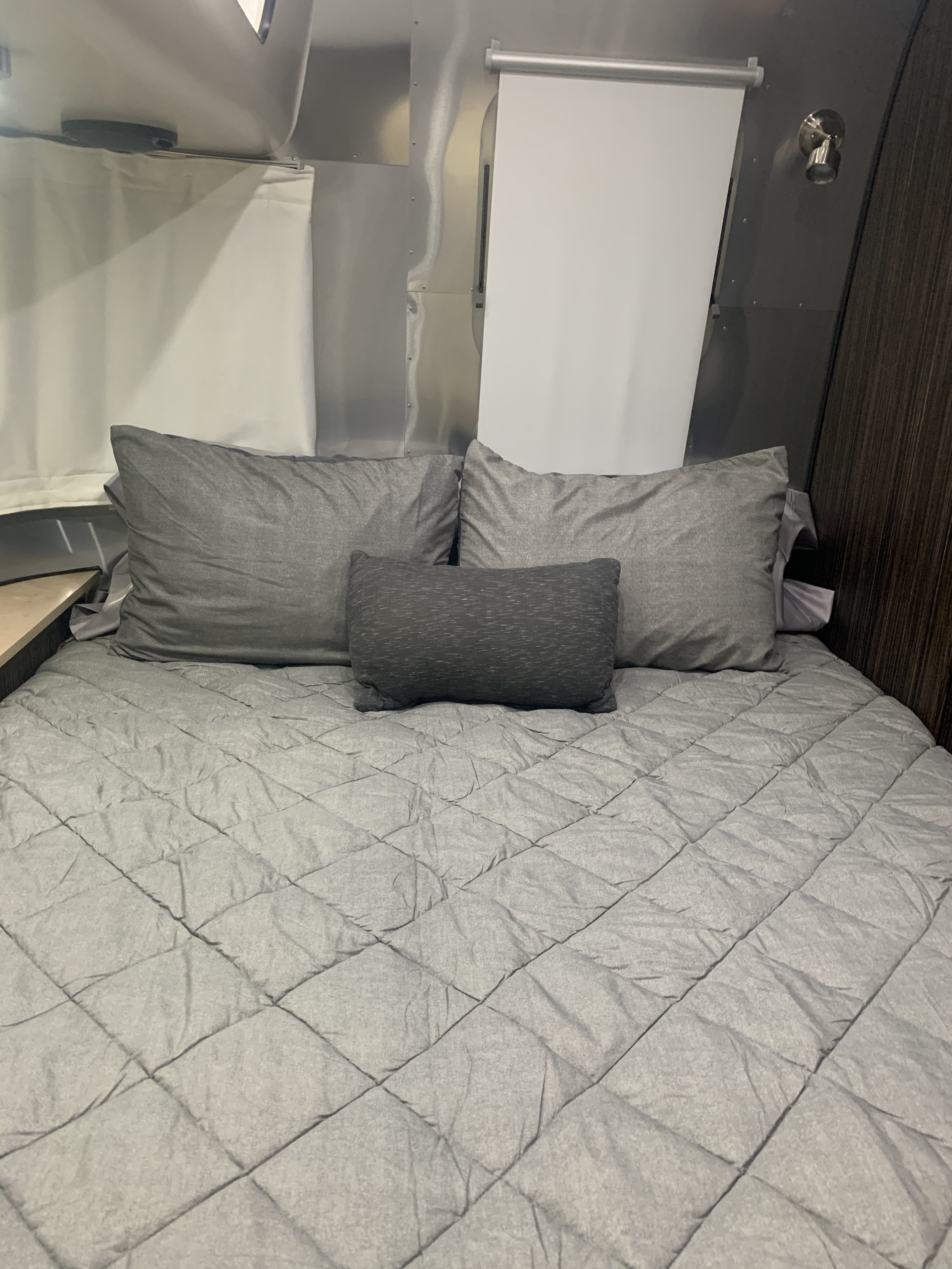 Cozy RV rental bedroom featuring a grey quilted comforter, pillows, and sleek silver walls with window shades.. Airstream International Signature 2019