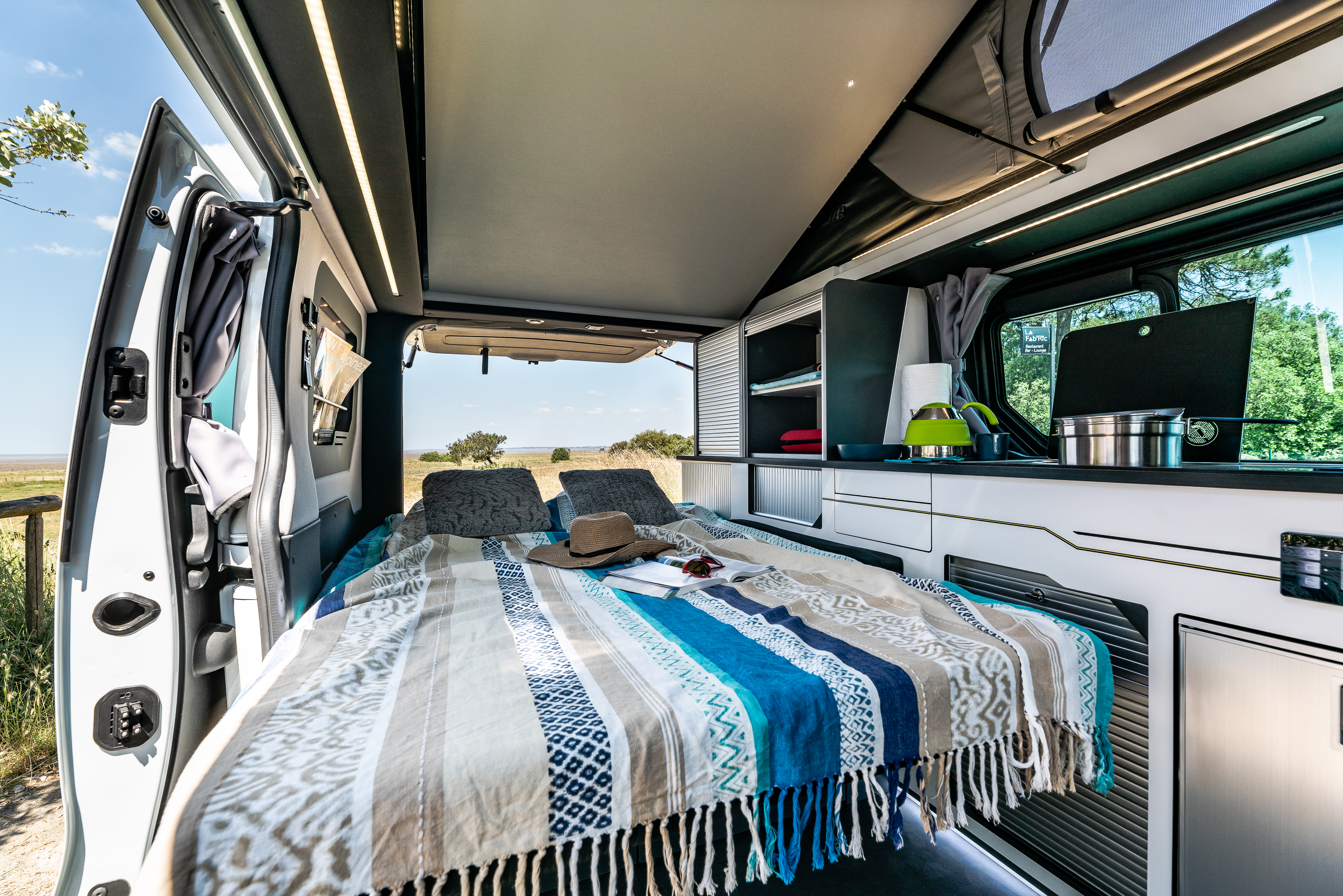 Cozy RV rental interior features a comfortable bed, compact kitchen, and scenic outdoor views for unforgettable trips.. Hanroad Trek 2023