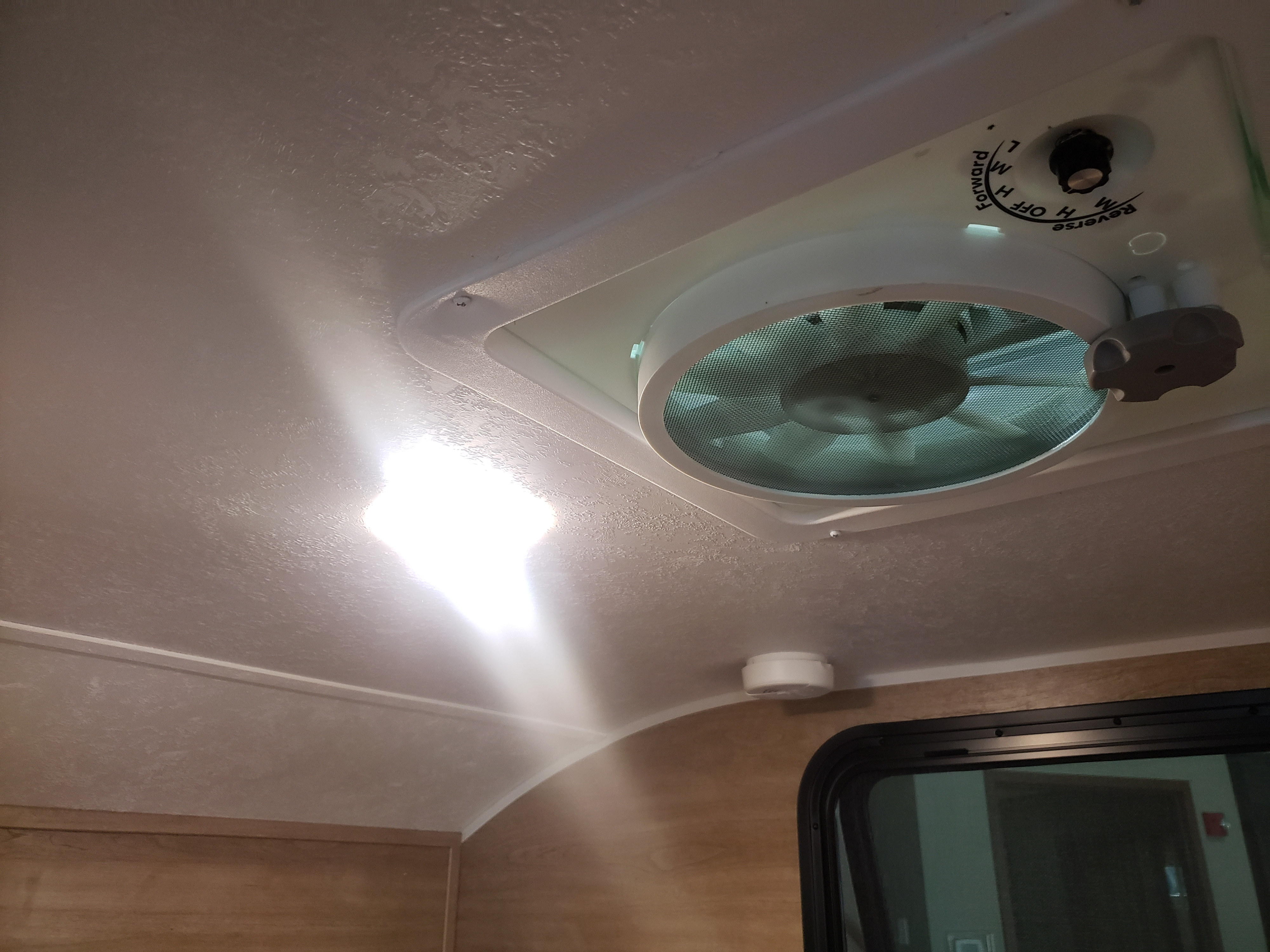 Overhead view in an RV rental: bright ceiling light, vent fan with controls, smoke detector, and window below.. Braxton Creek Bushwhacker 2021
