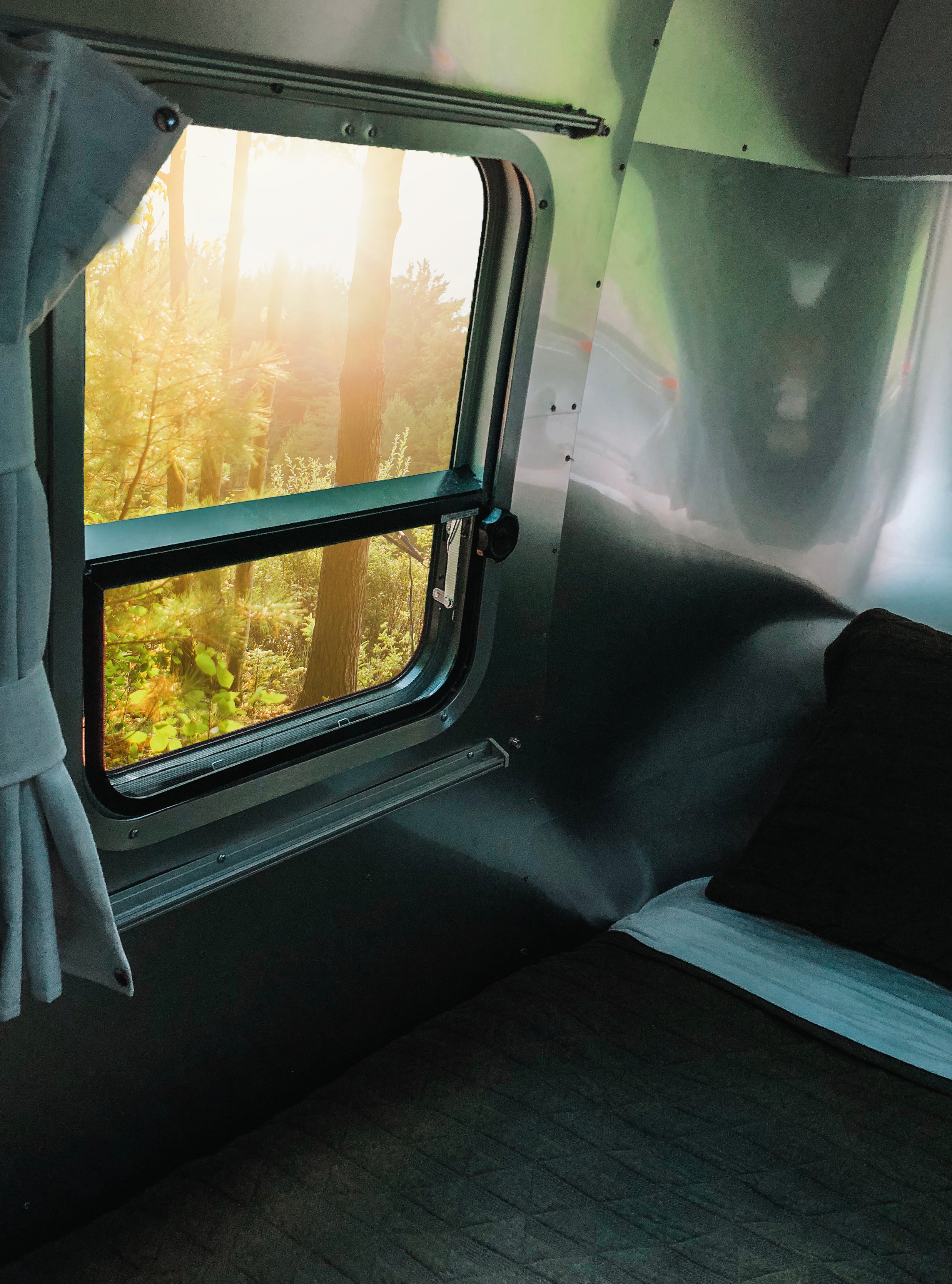 Experience nature with an RV rental. A cozy Airstream interior features a window looking out to a bright, sunlit forest.. Airstream Bambi 2021