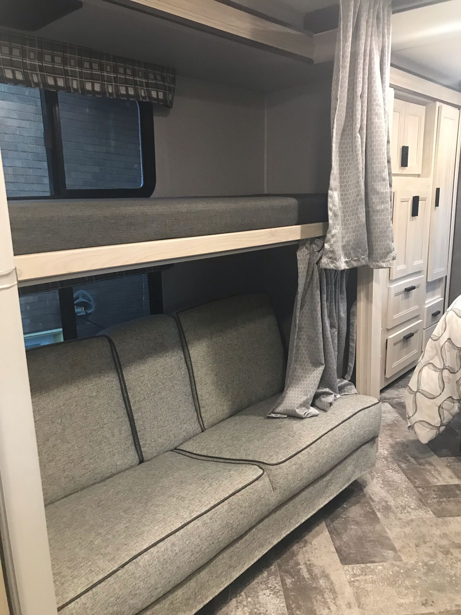 This RV rental interior features a grey sofa below an upper bunk bed, storage cabinets, and windows.. Forest River Sunseeker LE 2021