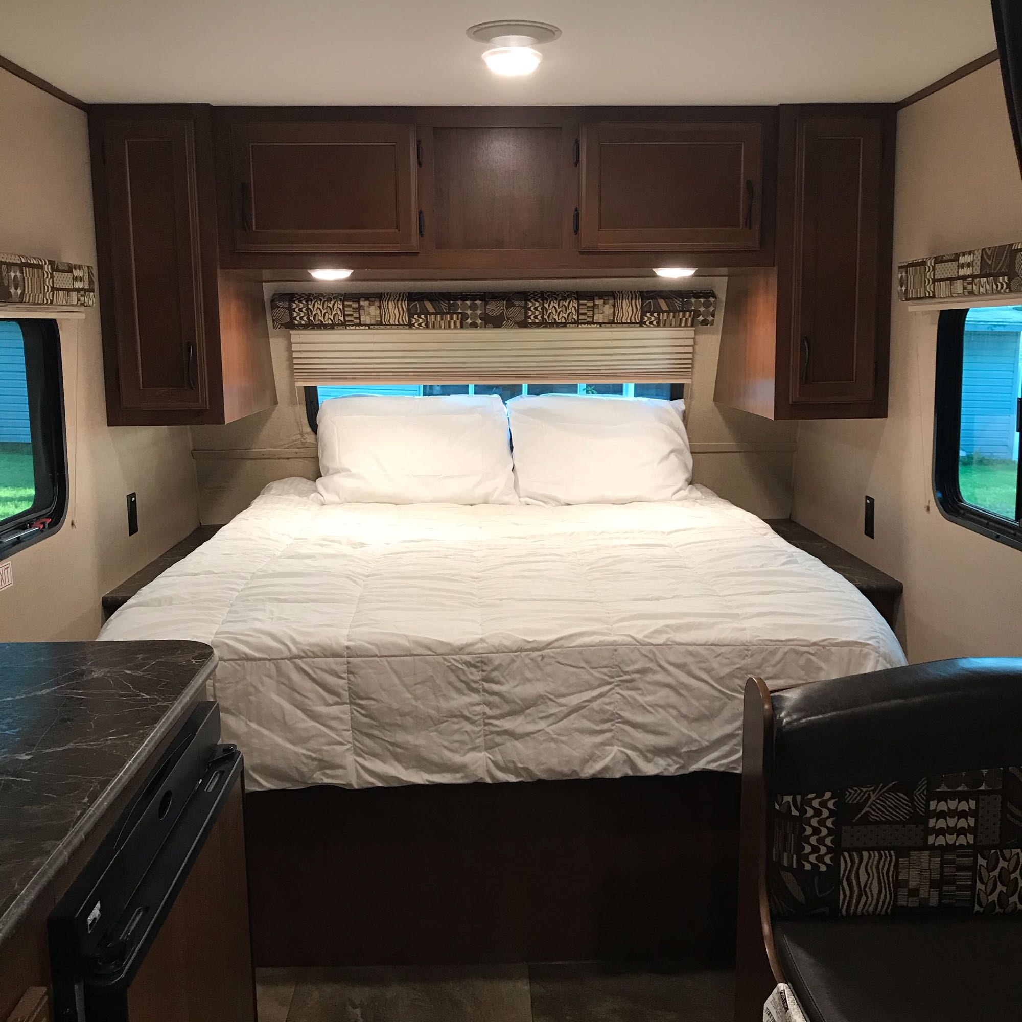 Compact RV rental bedroom featuring a comfortable bed, dark wood cabinets, and windows for cozy travel.. Jayco JayFlight 2016