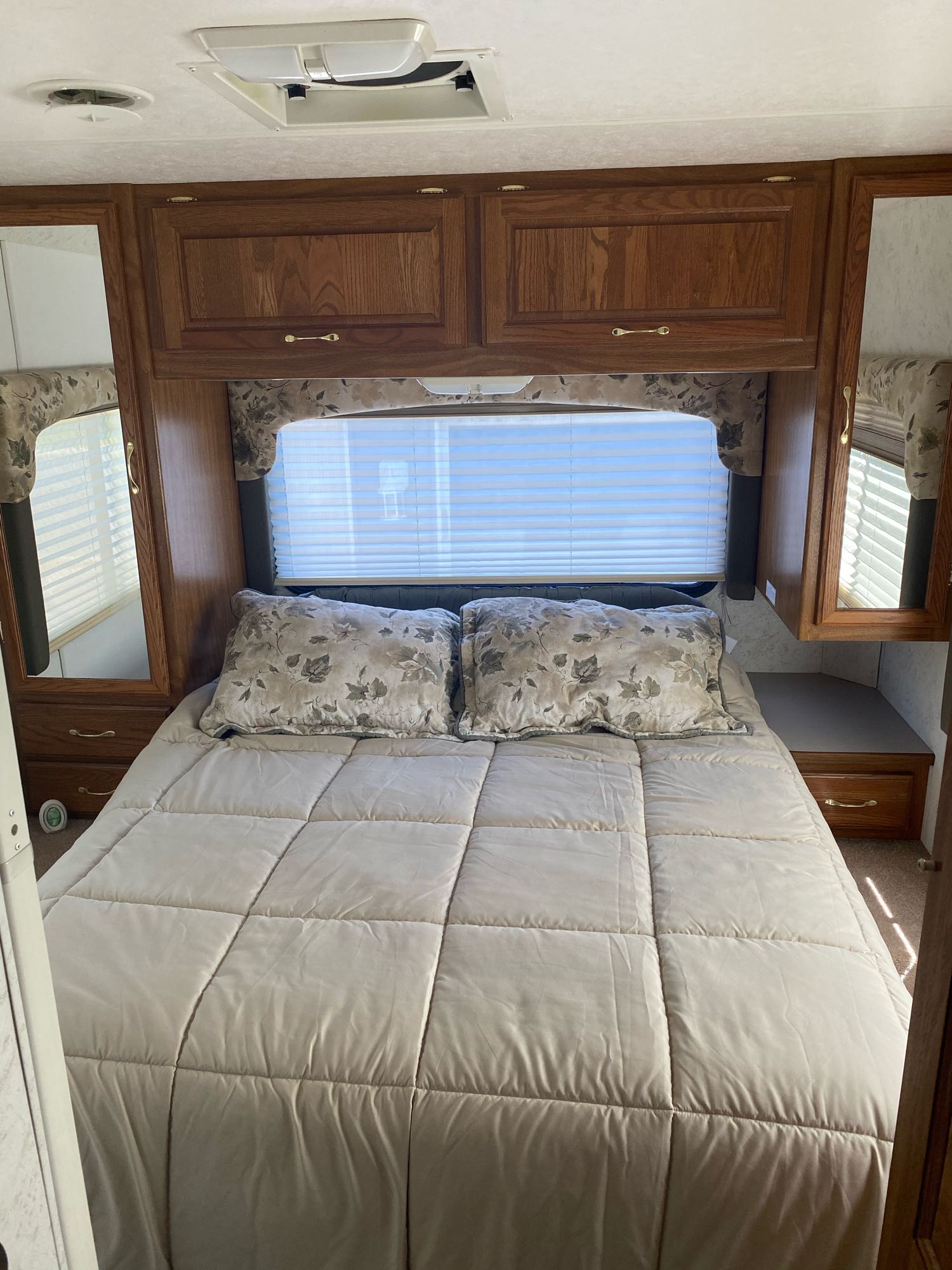 Comfortable RV rental bedroom featuring a queen bed, wooden cabinets, mirrored wardrobes, and window blinds.. Dutchmen Four Winds 2003